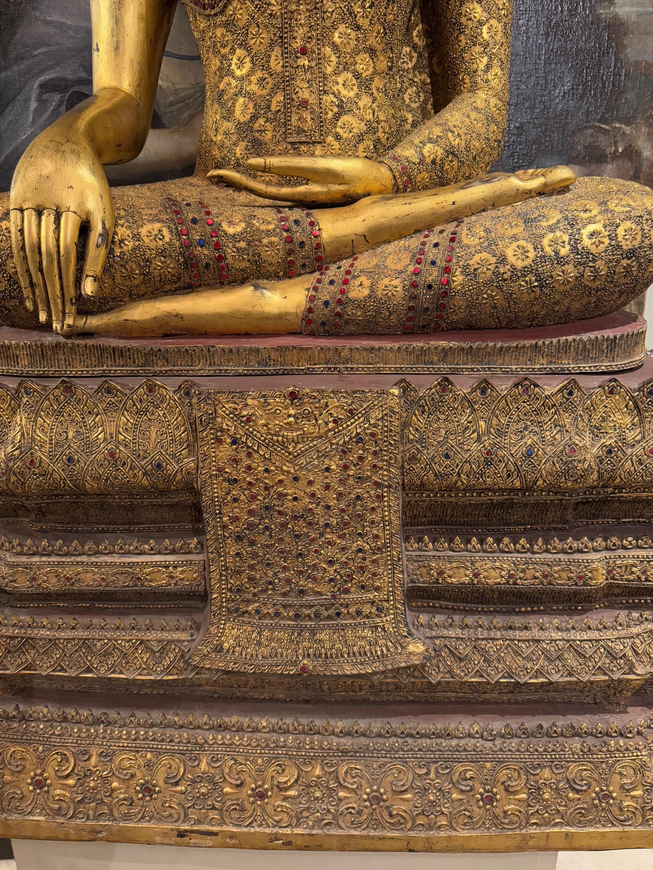 Très grand bouddha de style Rattanakosin, également connu sous le nom de style Bangkok, en bronze laqué et doré.
La présence de nombreuses pierres incrustées témoigne d'une forte influence birmane.
Le Bouddha représenté ici dans le Bhumisparsa