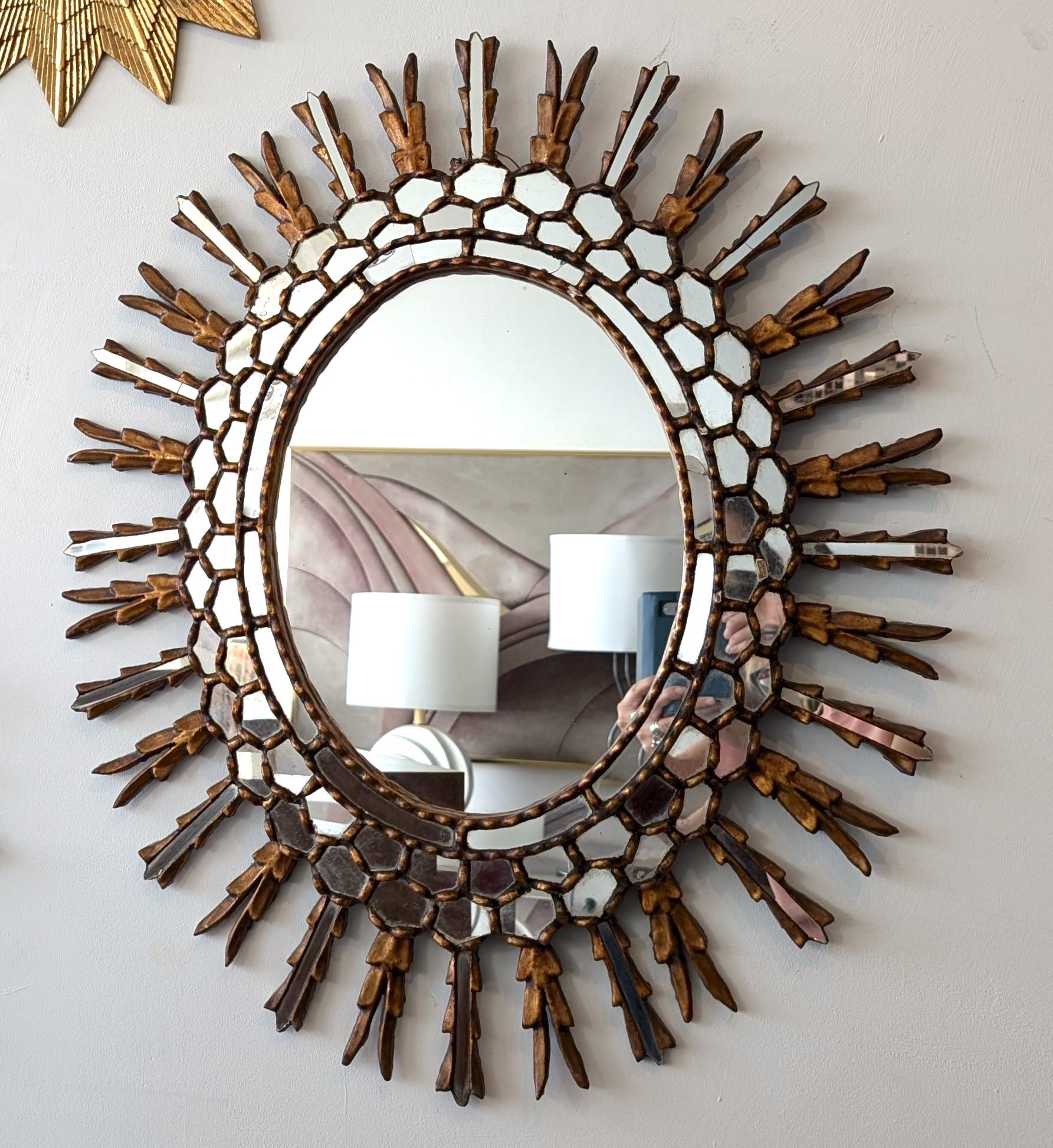 Très grand miroir espagnol en bois sculpté et doré, vers les années 1950, mais il pourrait être plus ancien. Présente de multiples petits morceaux de miroir autour du miroir central ovale et sur les rayons extérieurs alternés.
Quatre petites
