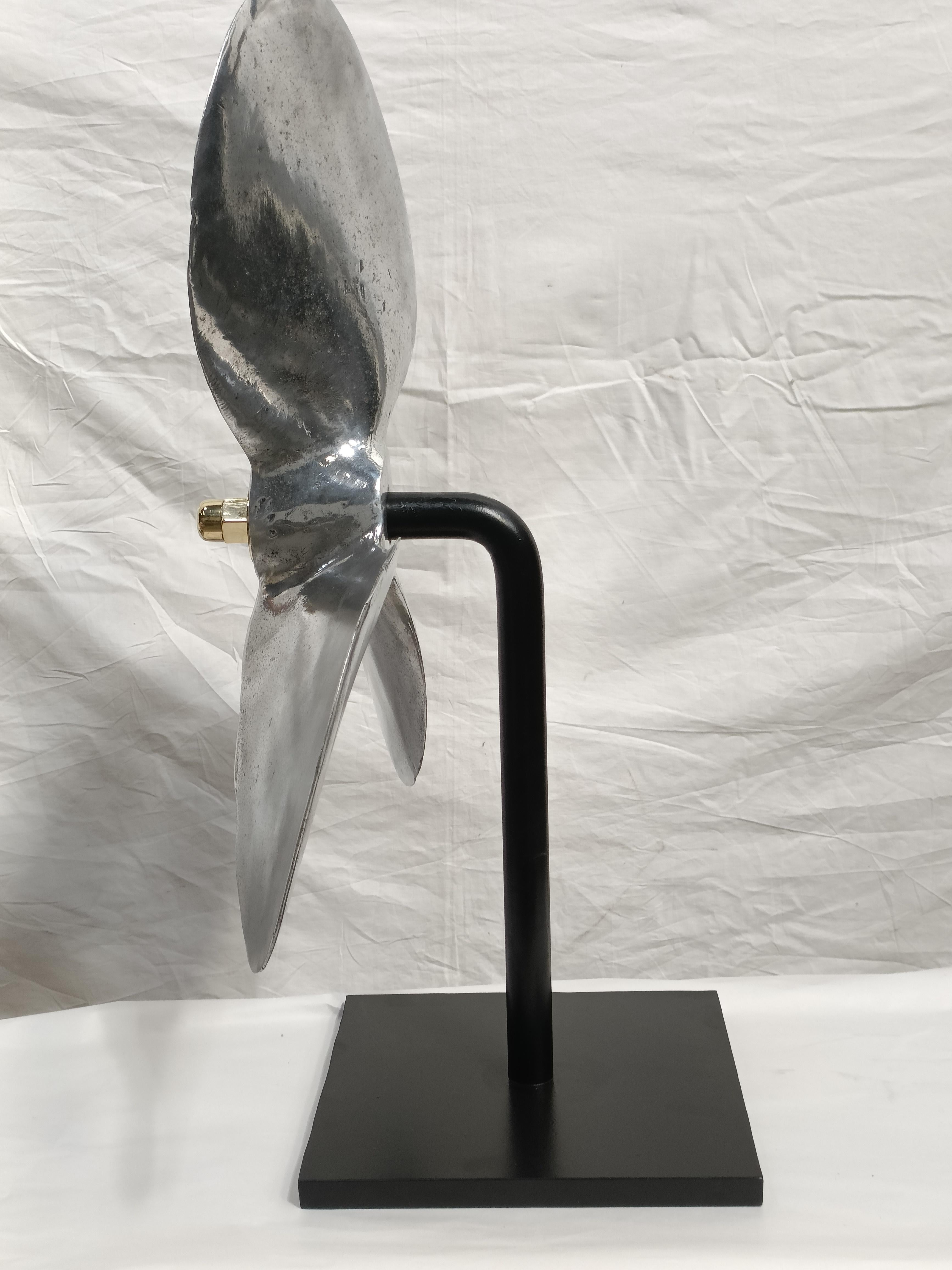 A very large chromed aluminum ship's propeller from a decommissioned lifeboat from the 1970's.  It has been mounted on an iron base to create a sculpture.  It is held in place with a brass knob.  Base is 12