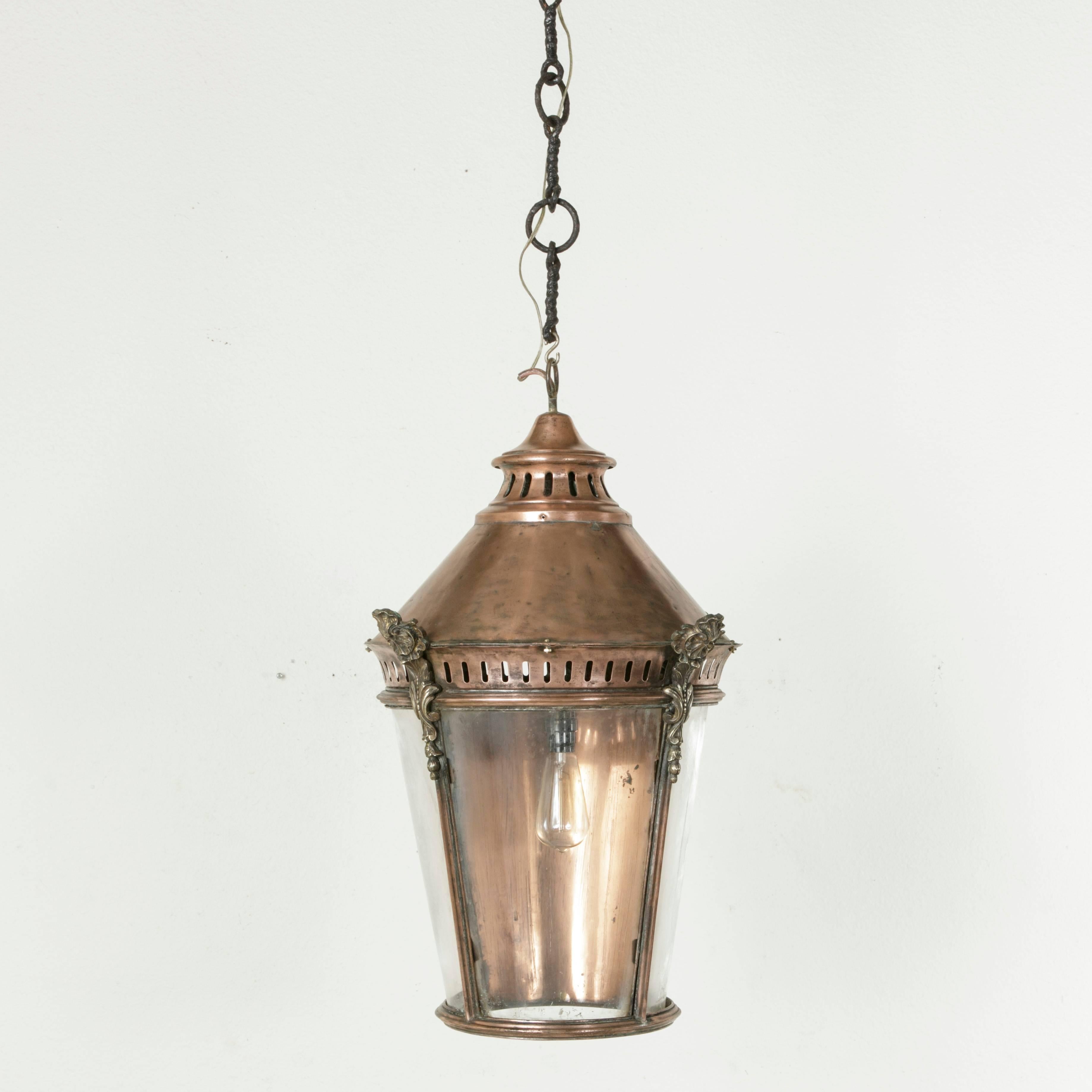 Originally hung at the entrance of a farm in Normandy France, this very large turn of the twentieth century copper and brass lantern stands at an impressive 28 inches in height. Suspended from a thick wrought iron chain, this piece features a solid