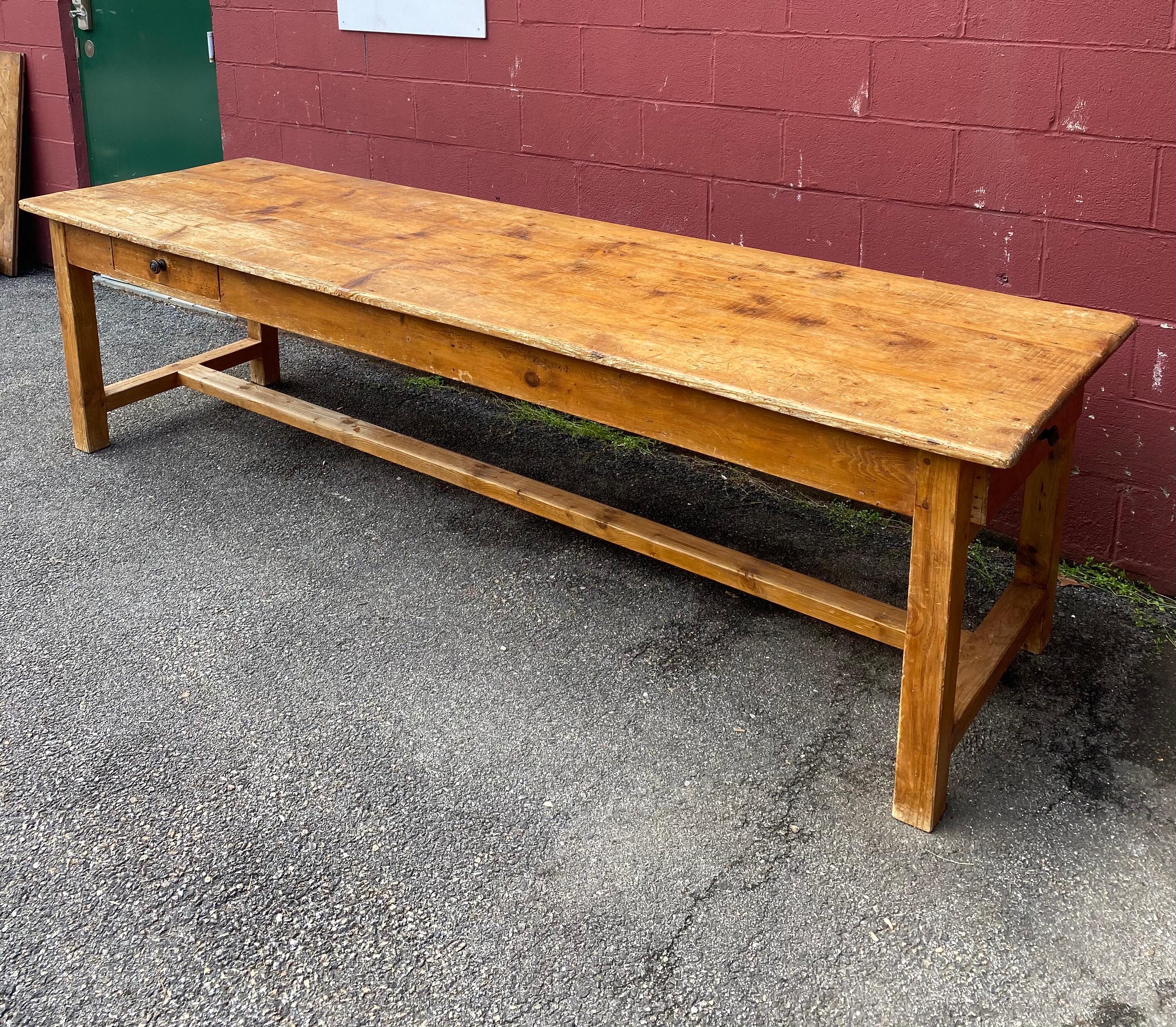Very large and massive work table made of sold pine. The table top is 3 solid planks each 113” long that shows years of use in a rich natural patina. The top is mounted on squared legs and a matching stretcher. There are 2 drawers, a very large one