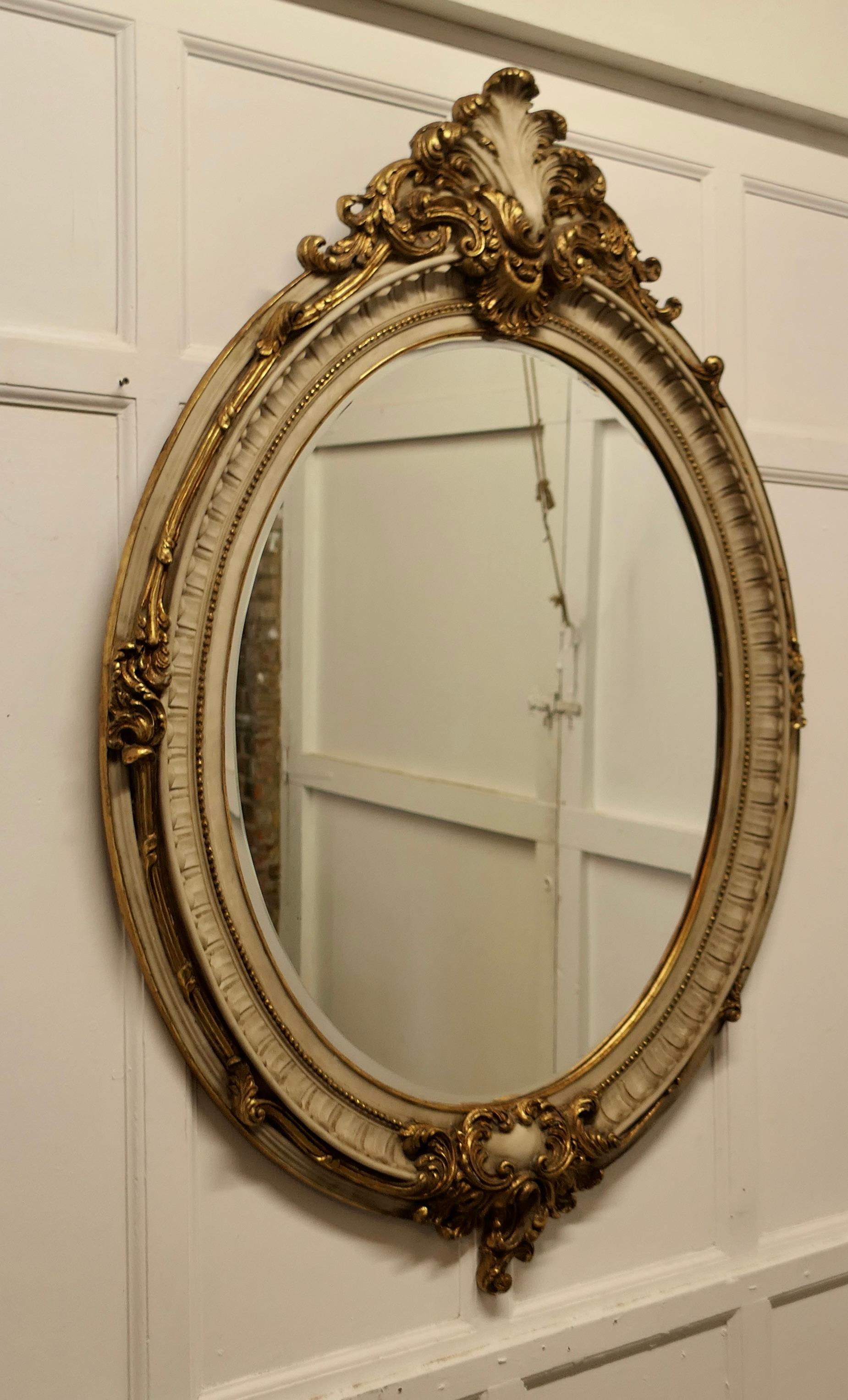Very large French Rococo style oval gilt wall mirror.

The mirror has an impressive 6” wide gilt frame in the Rococo Style, it is made in a simulated marble decorated with very large shells and scrolls in aged gilt
The oval frame is in good