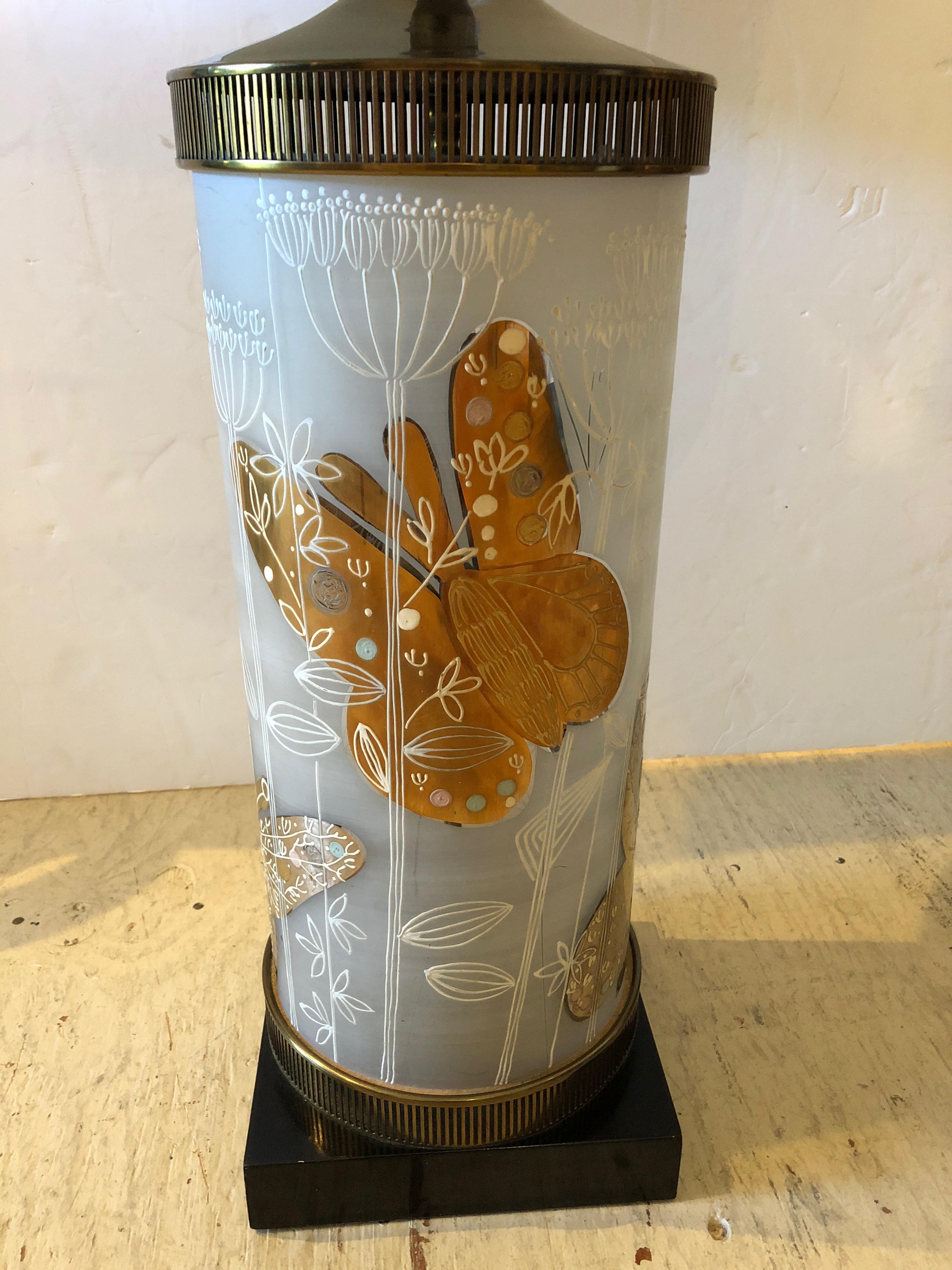  Mid-Century Modern lamp having a cylindrical shaped white etched glass base adorned with gold butterflies and white abstract trees. Brass on top and bottom and a handsome ebonized wood platform.