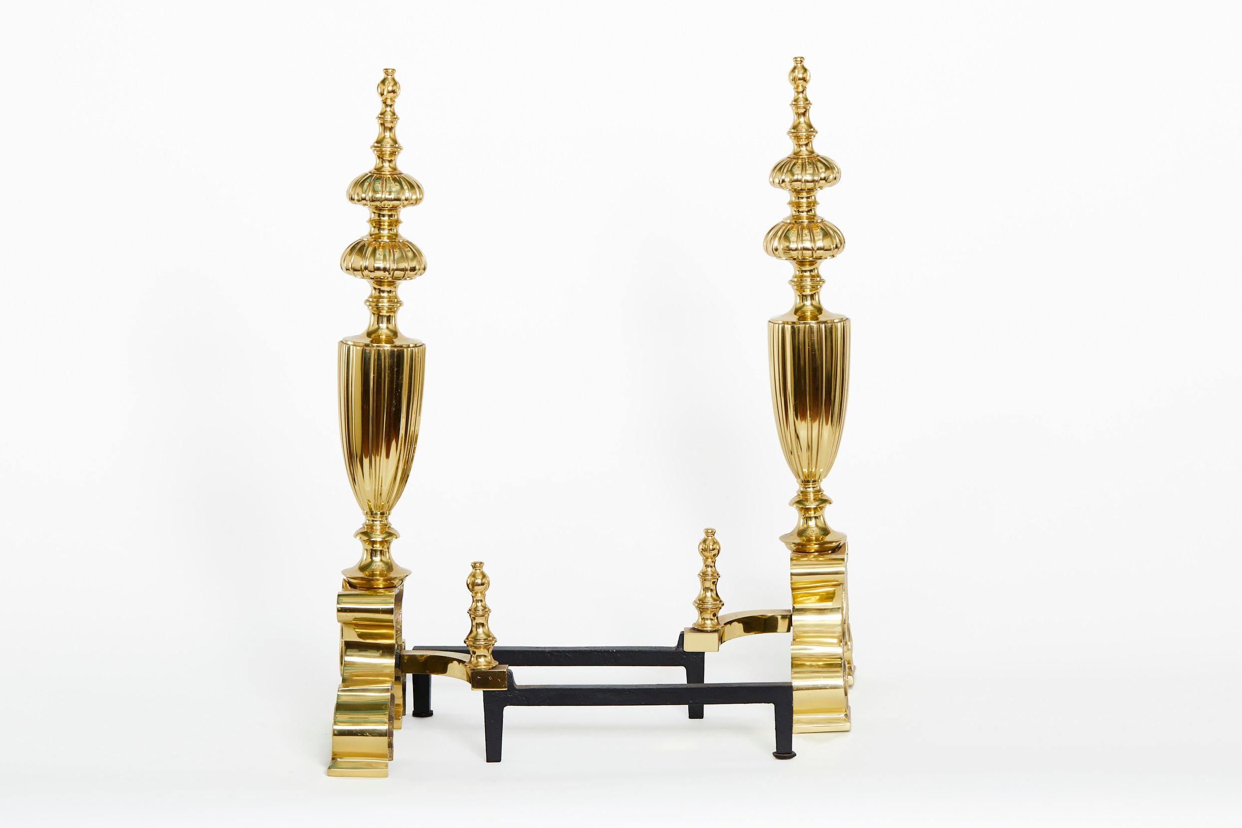 Very large and handsome solid brass Georgian style pair andirons with urn design details top and exterior feet details. Each andiron is in great condition. Minor wear. Each one measures 28 inches high X 12 inches wide X 19 inches deep.