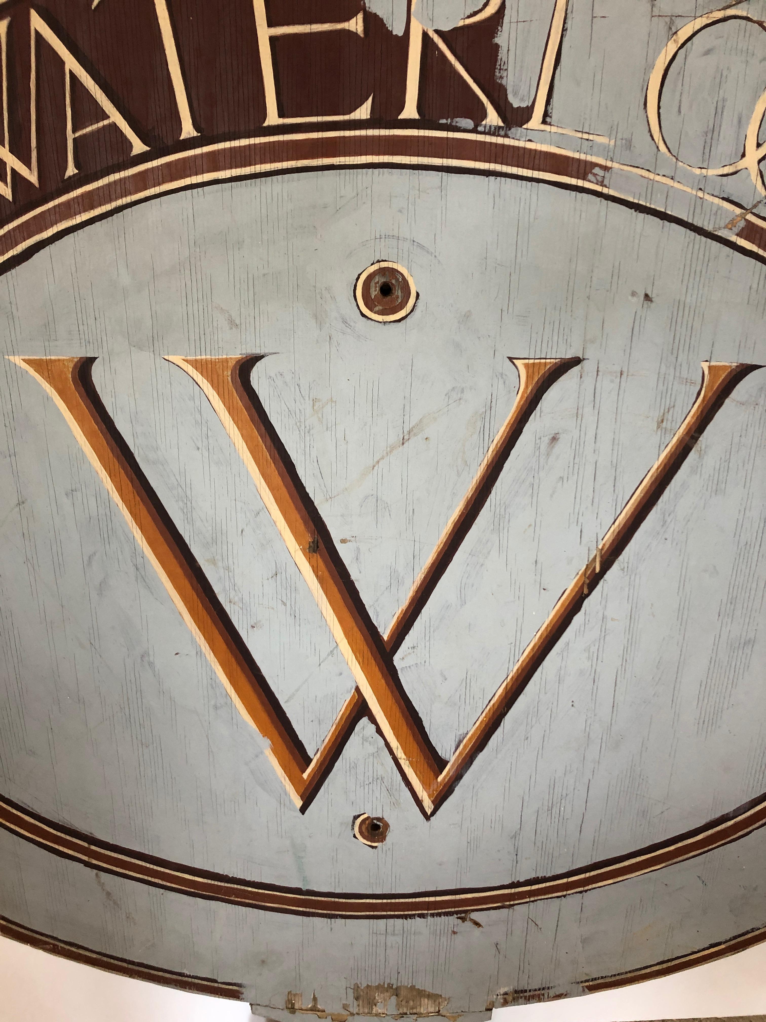 A large wonderfully shaped French blue grey wooden sign with a central letter W and a partially obscured or unfinished waterloo spelled out at the top.