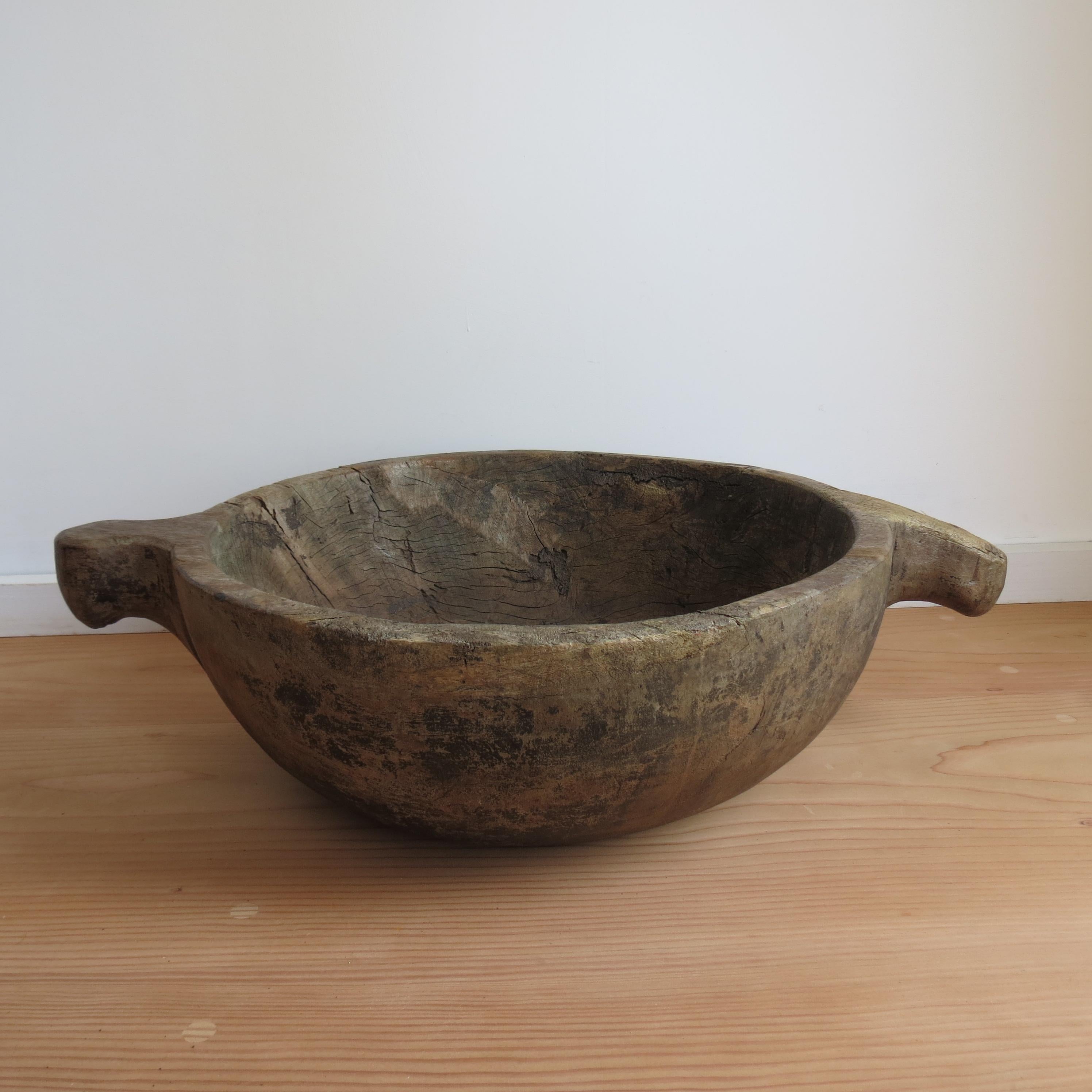 A very large rustic wooden bowl with two handles originally from the early 20th century. One solid piece of wood has been hand carved, with a decorated handle either side of the large bowl. Originally from Africa. Very much in the Wabi Sabi Style,