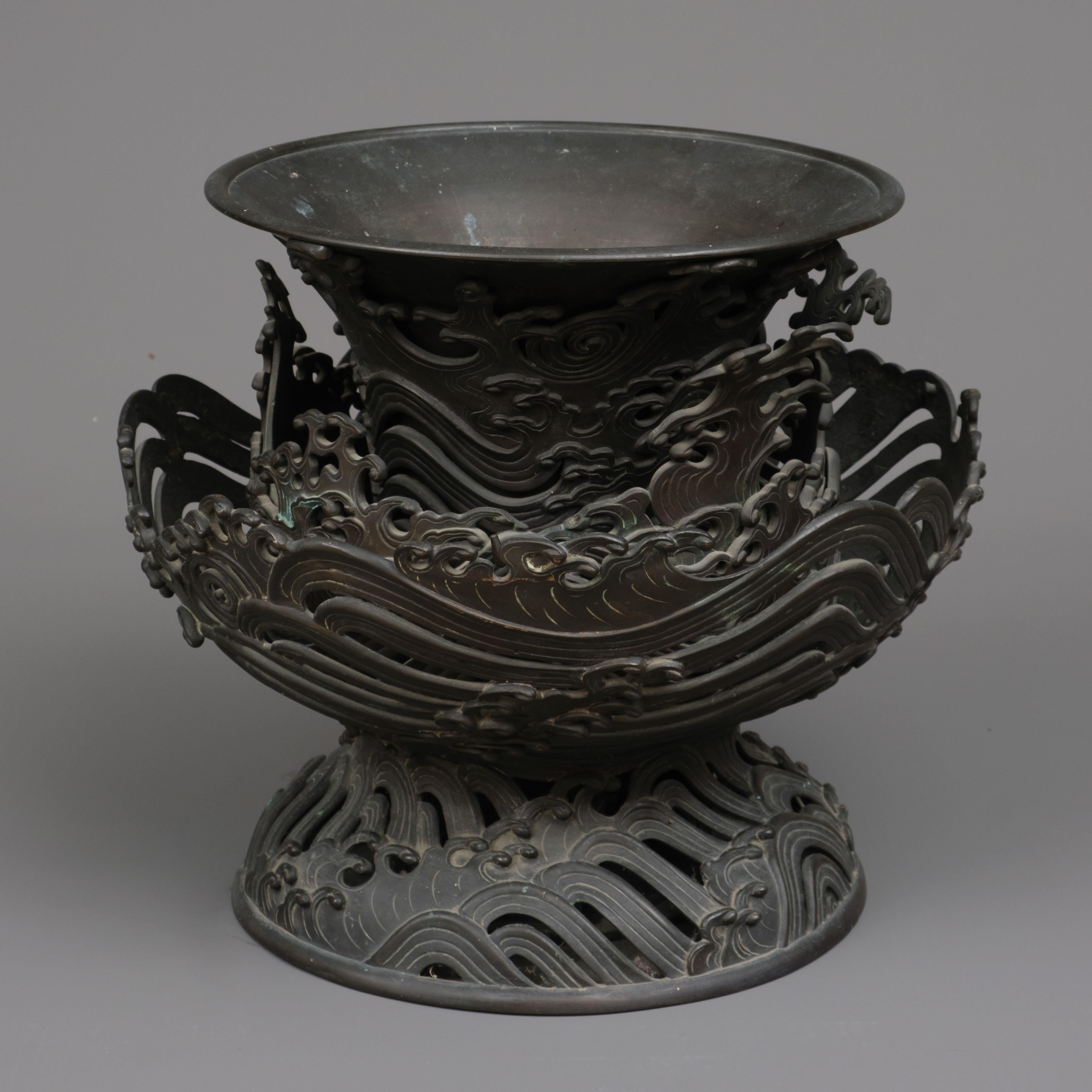 Remarkable and very large bronze 4-tiered trumpet vase intricately designed with a motif of tumultuous waves.
It’s crafted to give the impression that the trumpet-shaped chalice, is engulfed by outward expanding layers of waves rising upwards from