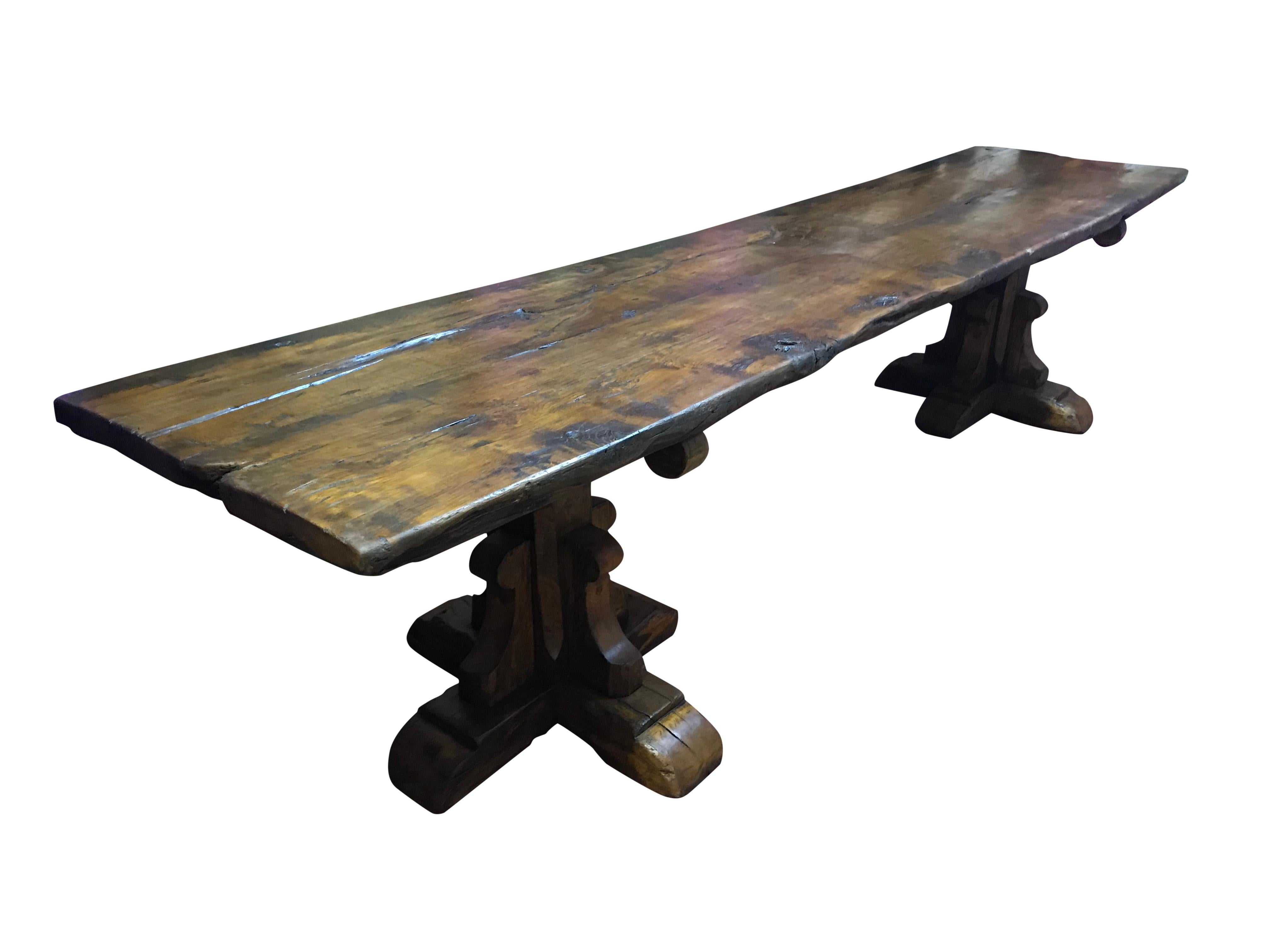 A very large medieval style golden oak rustic refectory table with a double plank top, supported by two square 'X' frame pedestals.
