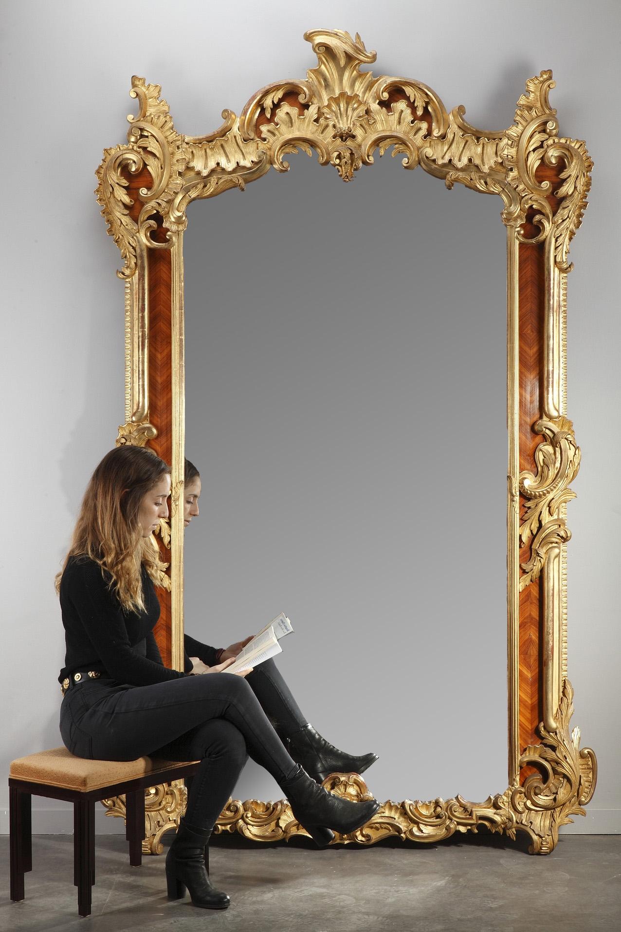 This monumentally-sized Louis XV-style Revival mirror features an undulating, intricately carved giltwood frame on rosewood veneer background. Designed in Rocaille style, the mirror boasts foliate decoration of acanthus leaves, C scrolls and shell
