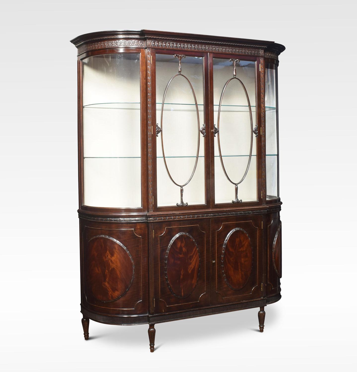 Mahogany bow ended display cabinet the cornice having Greek Key moldings above two large rectangular doors, flanked by two bowed glazed sides. The base section having four flame mahogany oval panels with two central doors enclosing large storage