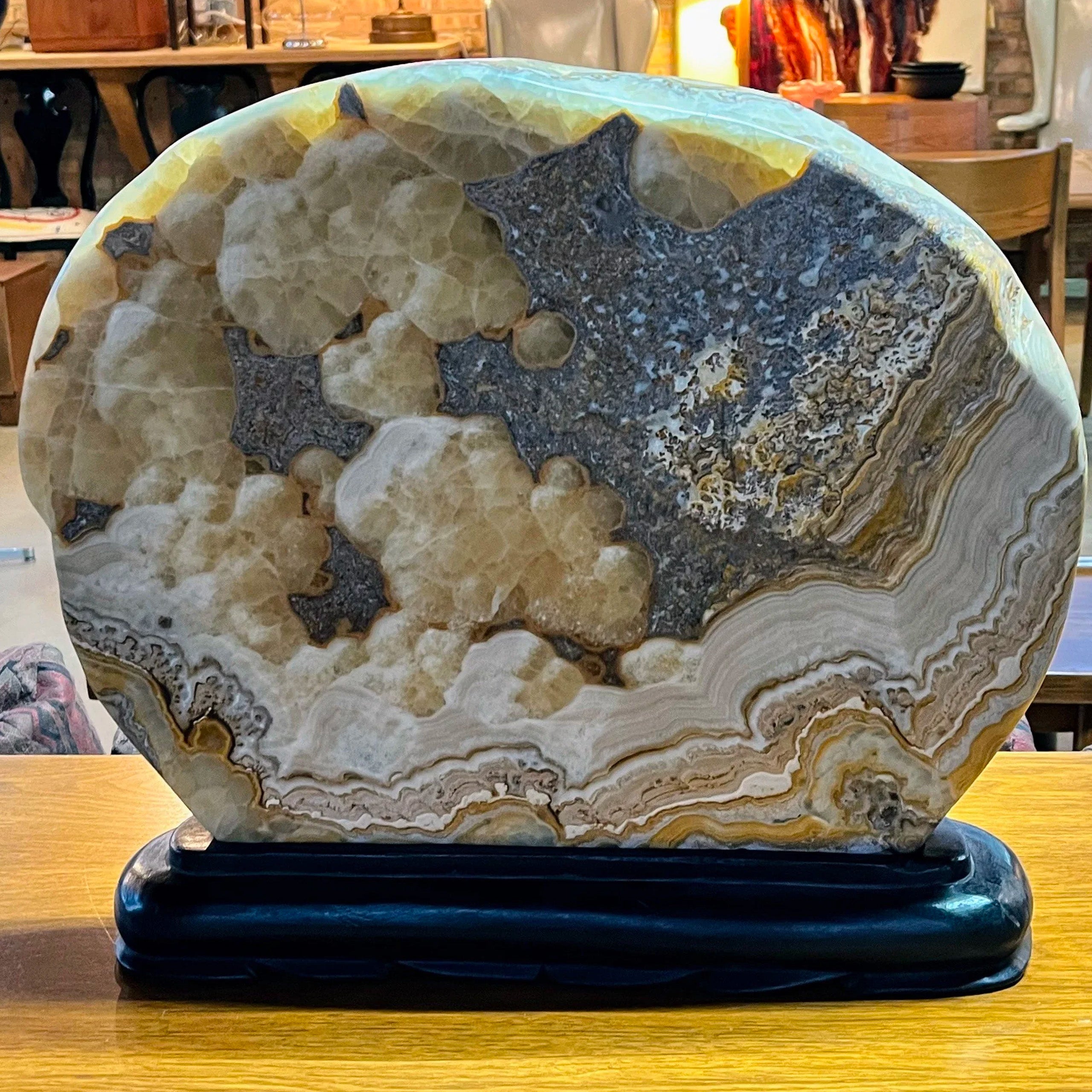 Very Large Natural Onyx Stone Sculpture on Carved Wooden Base

A large and visually striking polished slice of natural onyx, displayed on a custom carved wooden stand. This is a sculptural organic piece, with rich patterns of color and movement