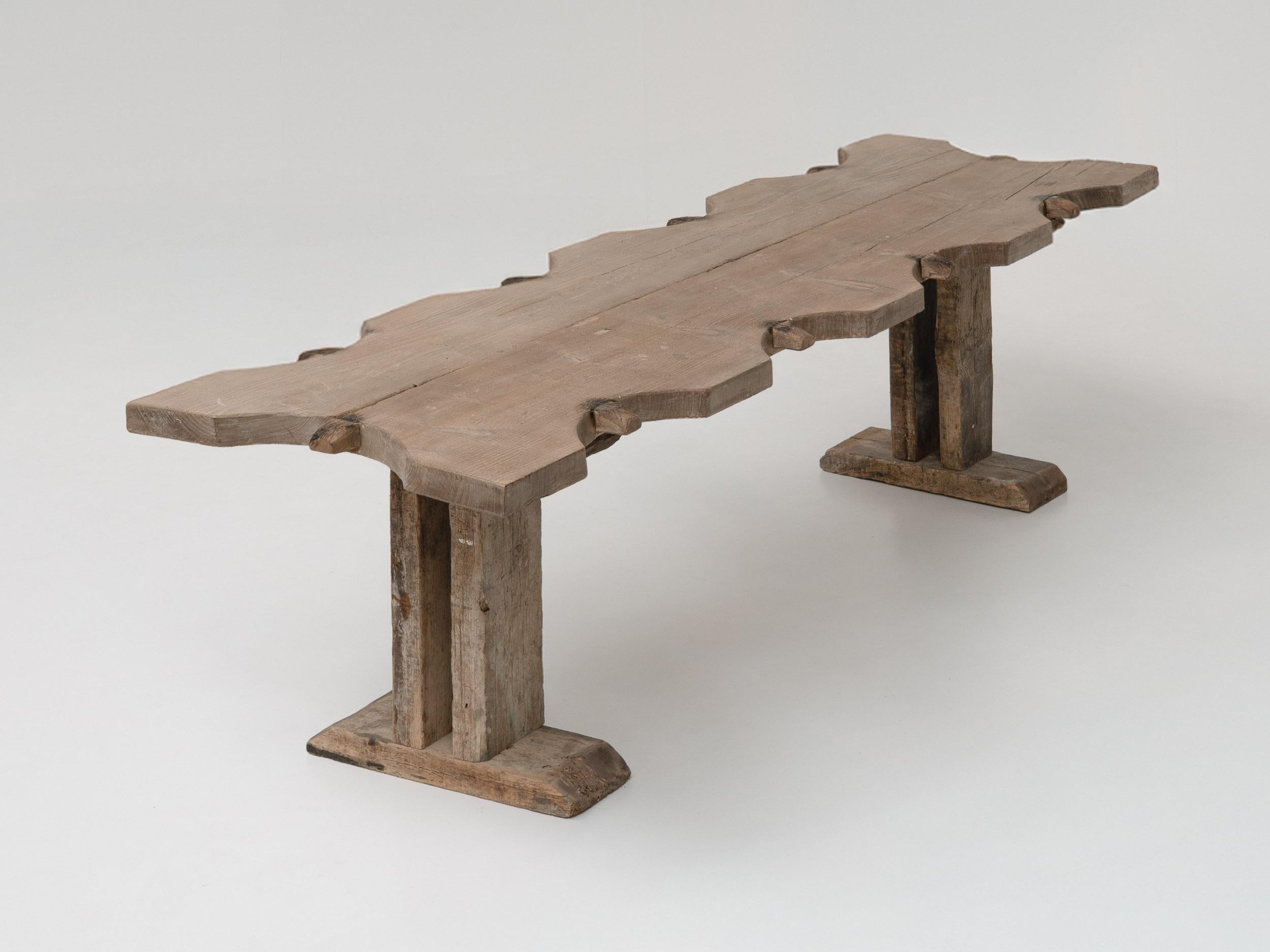 Cette grande table de salle à manger de ferme vintage provenant de France allie harmonieusement le charme rustique à une sensibilité moderne. Fabriquée à la main en bois massif vieilli, son plateau sculpté de façon unique et sa base architecturale