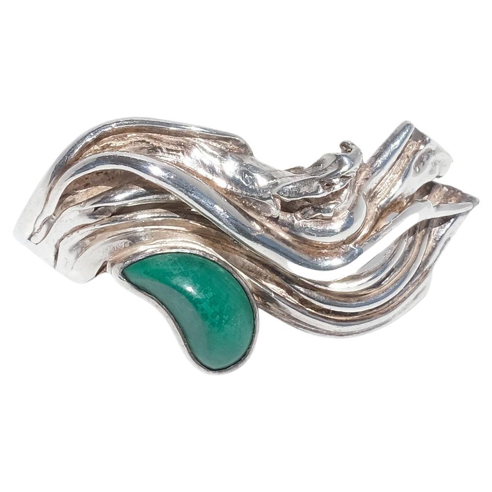 This sterling silver ring is adorned with a tear-shaped malachite and an undulating silver wave. Its shaft is prominent.

This brutalist ring has amazing structural and textural elements and in our opinion it radiates freedom. It is an eye-catcher.