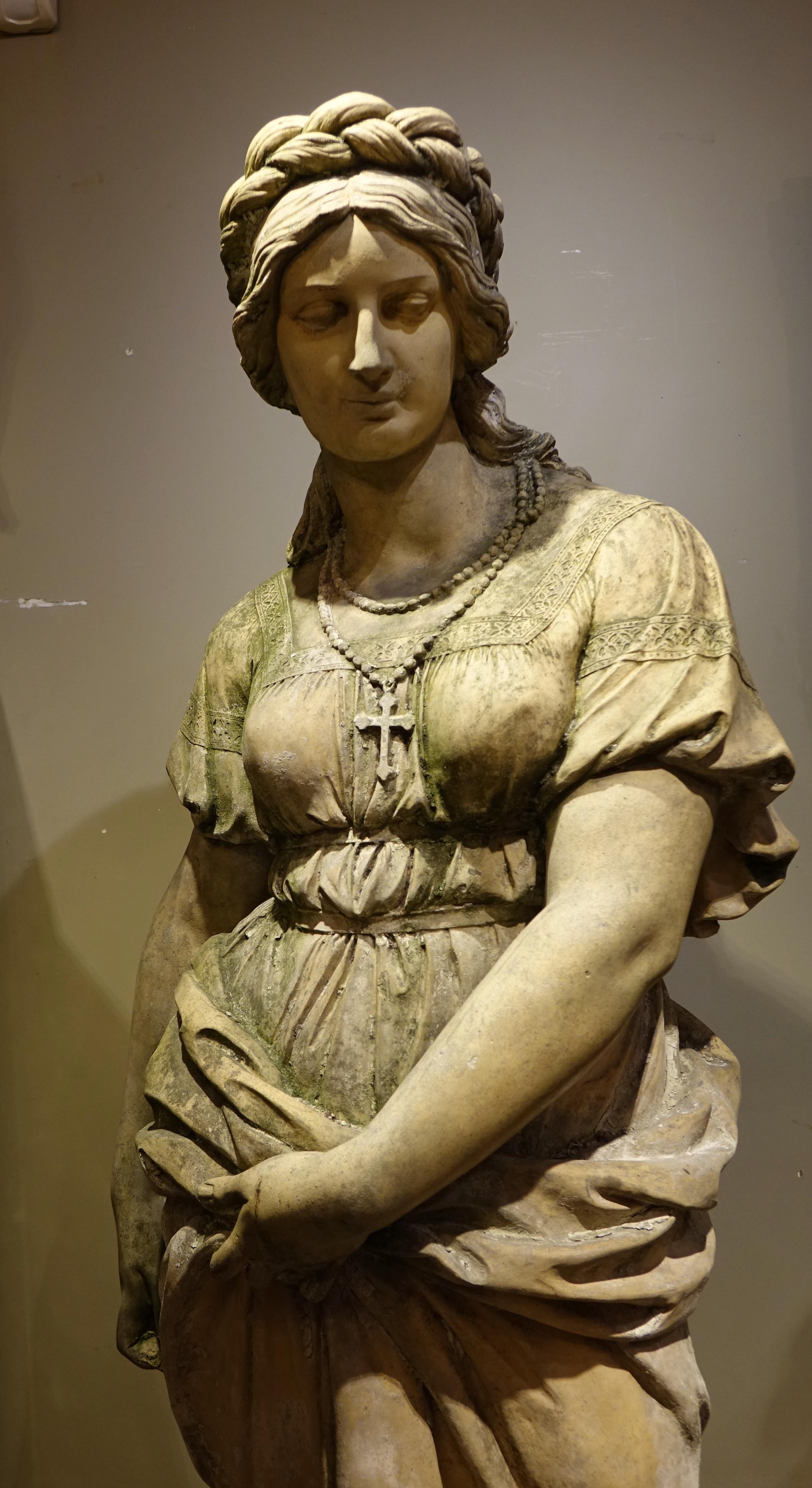 Very large terracotta ( 1.70m) depicting a young woman raising her garment slightly with her left arm to climb down from a rock.
The right arm close to the body, the hand must have been holding a missing element.
Her hair is braided, accentuating
