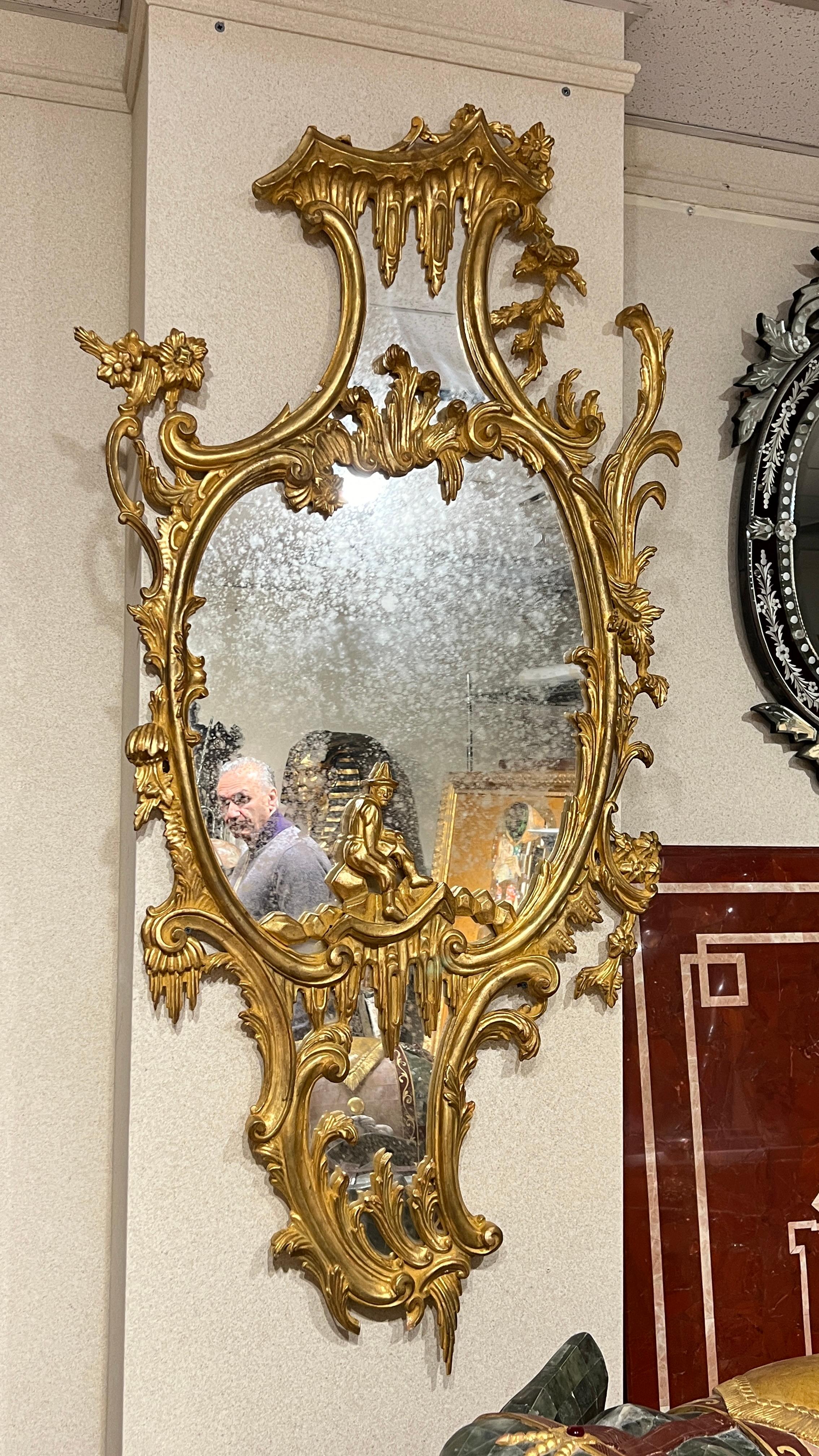 Italian made, large  giltwood mirror in the Chinese Chippendale style, measuring 33 by 65 inches, featuring stylized foliate scrolls and rocaille designs and Chinese figure.