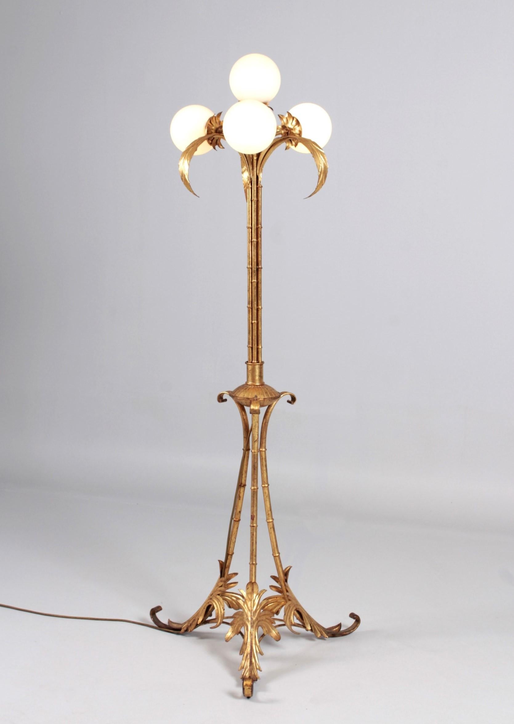 Beautiful and very large vintage floor lamp made of gold-plated brass.
Seven bundled bamboo or palm trunks grow upwards in a straight line on a three-legged base decorated with leaves. Three of the trunks end at the top in beautifully detailed palm