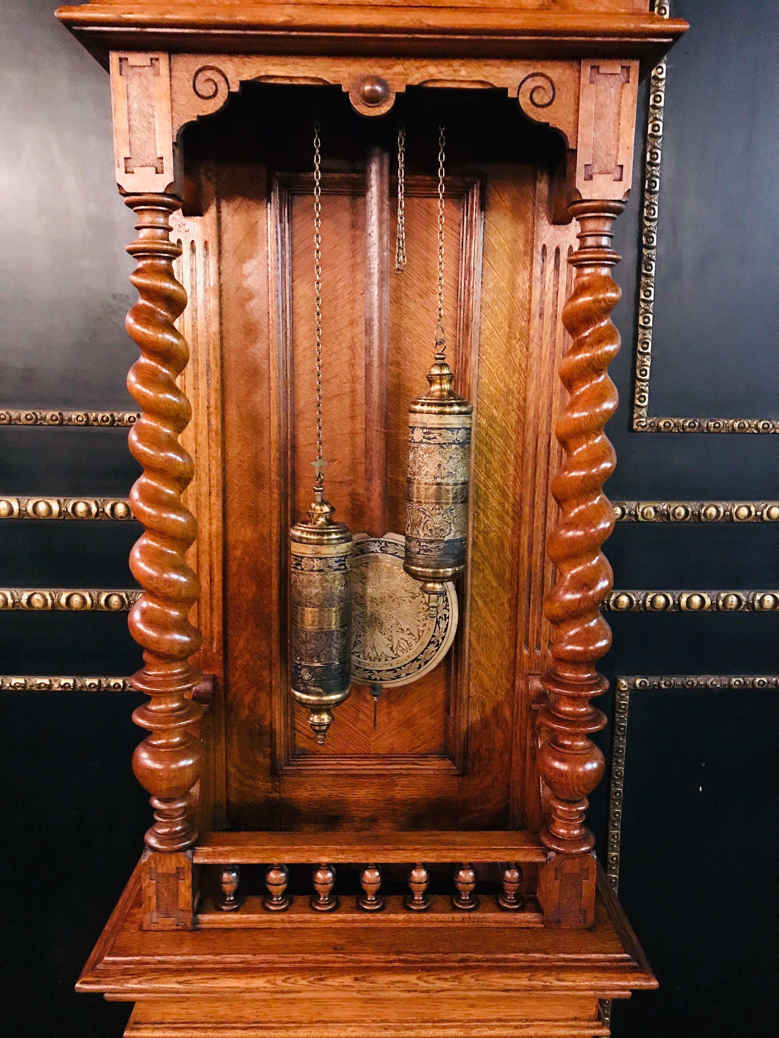 This beautiful piece dates from circa 1860.

The material is oak.
Headboard with a door that can be opened and small inspection flaps to the side.
Outside the glass are wood ornamentation.
The clock has very nice round columns.
Very nice pendulum