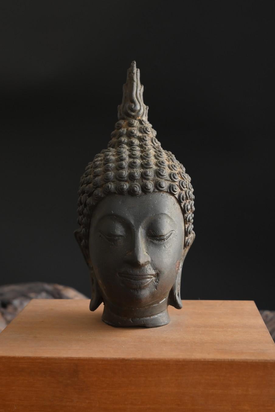 This is the head of a bronze or brass Buddha statue made in ancient times in Thailand.
It is thought that this Buddha statue was made from approximately the Sukhothai period to the Ayutthaya period.
It has an egg-shaped head, arched eyebrows,
