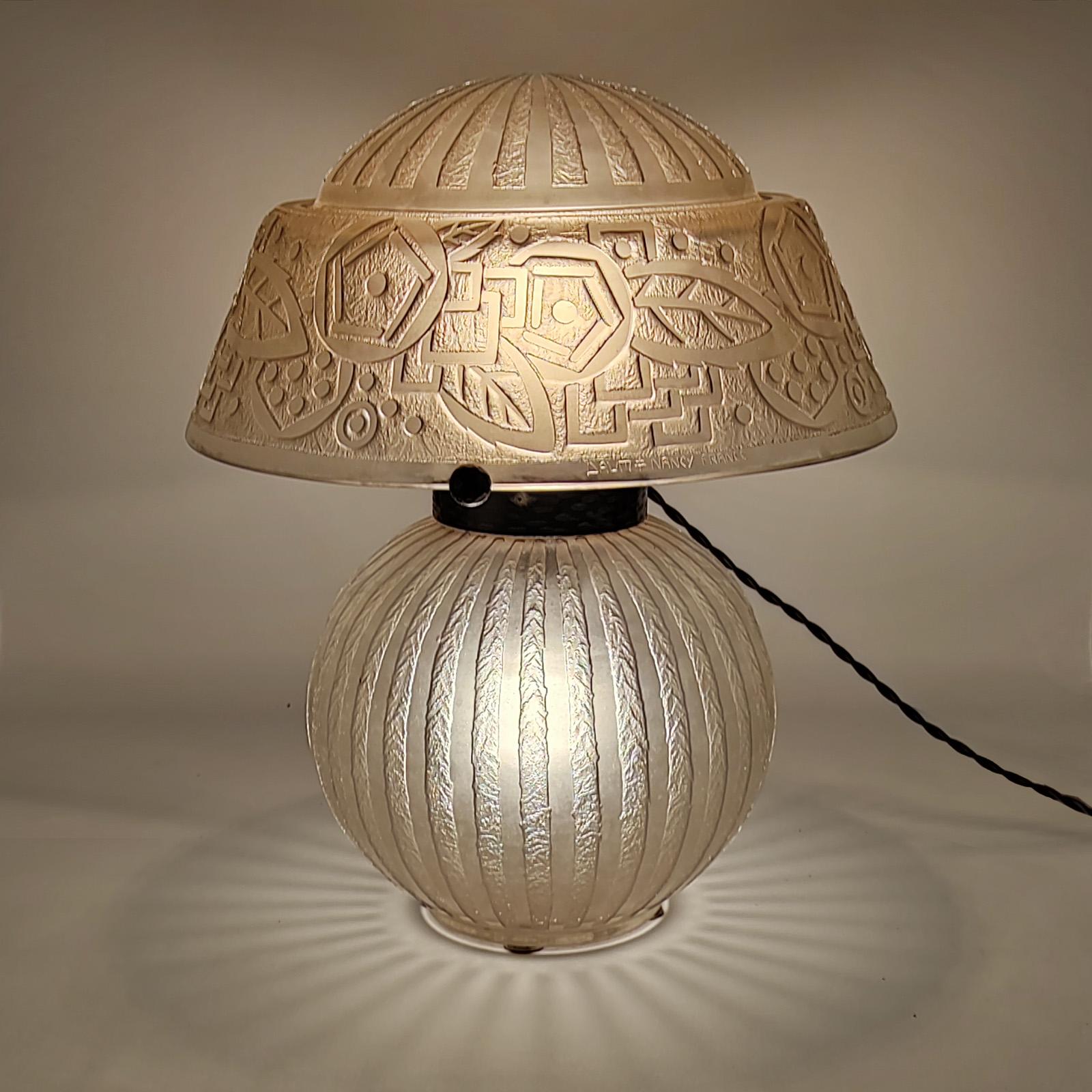 Art Deco Daum Freres Nancy table lamp.
Colorless smoky pinkish glass, etched ice-mat, with a geometric pattern.
Three arms in chromed hammered wrought iron holding the shade.
Electrified, two bayonet sockets, foot illuminated.
Foot and lamp-shade