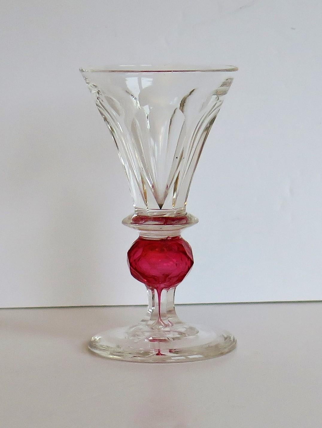 This is a rare hand blown drinking glass with a most unusual stem having a colored cranberry glass ball knop and further cut detail, made in England during the mid Victorian period of the 19th century, circa 1860.

The glass is hand blown with a