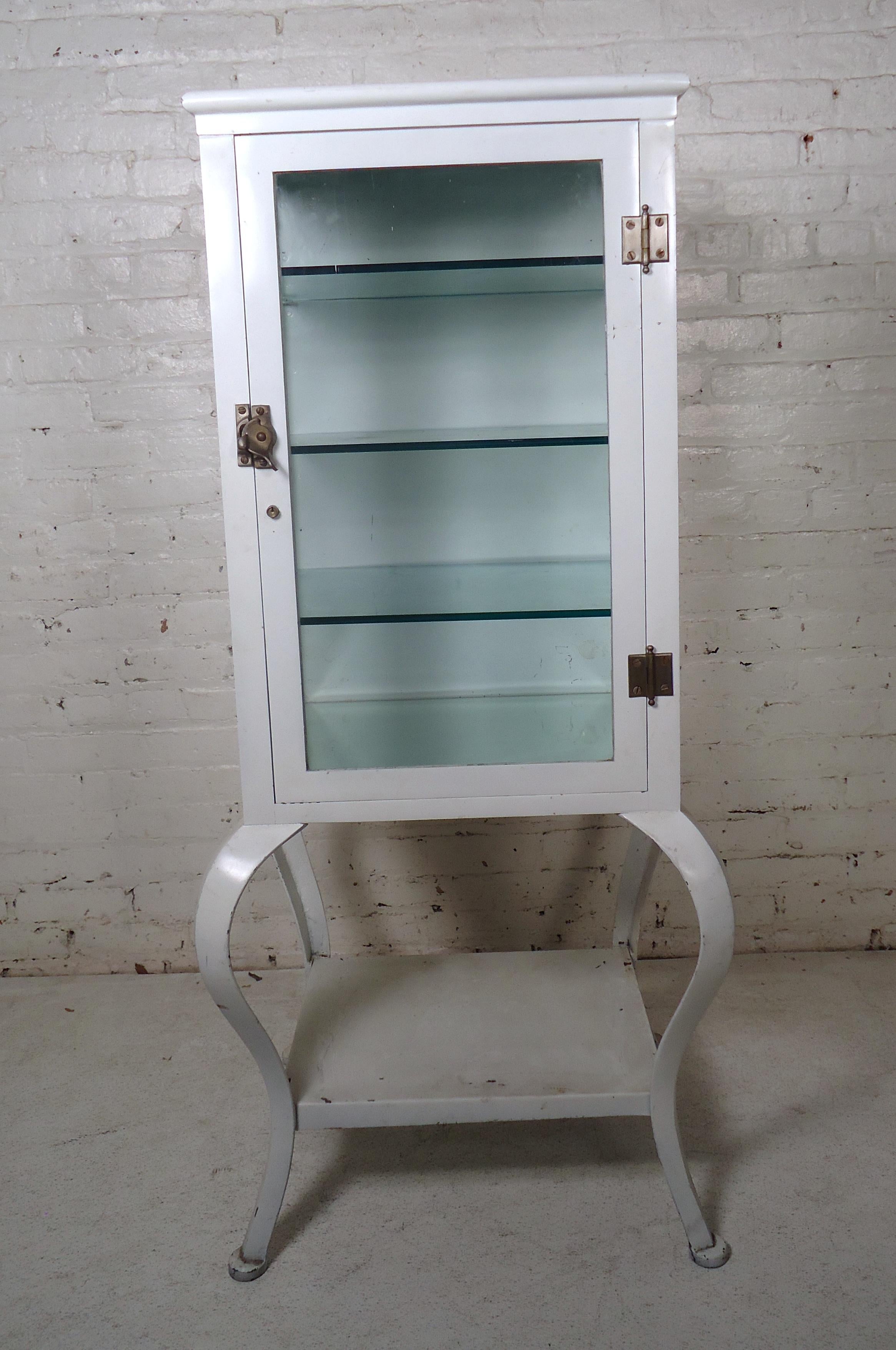 This vintage industrial medical cabinet features steel construction with wide glass display windows. Unique legs and shape make this stylish steel vitrine a wonderful storage piece in any interior. Please confirm item location (NY or NJ), two glass