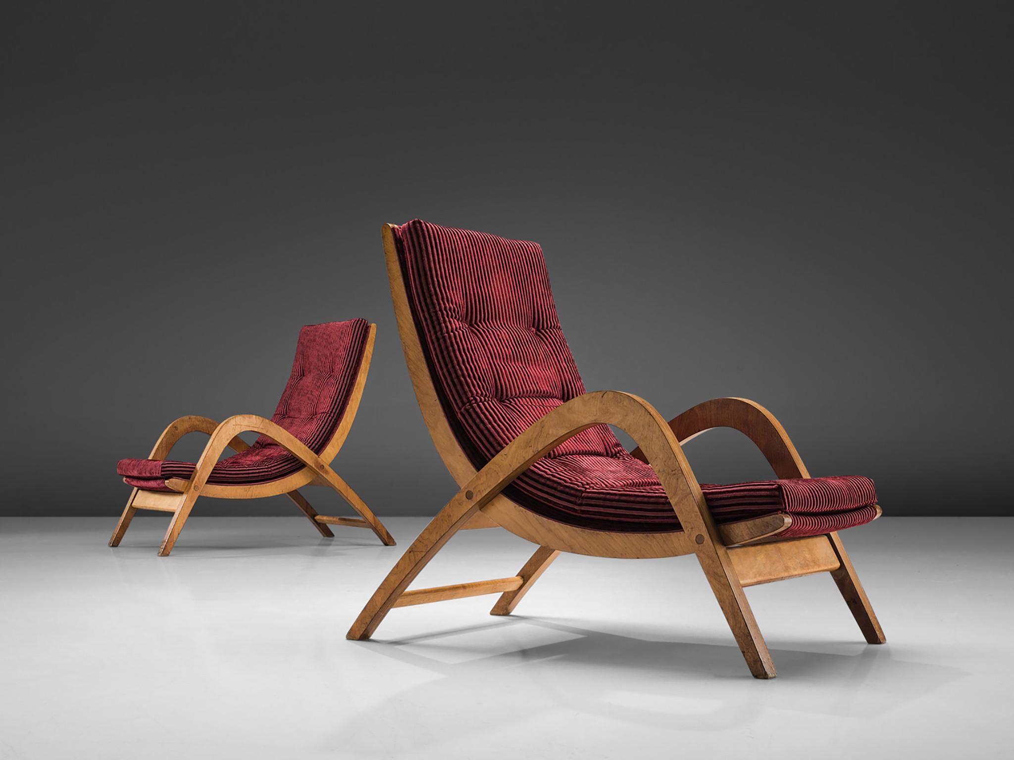 Neil Morris for H. Morris, lounge chairs, burgundy red upholstery and plywood, Scotland, 1940s. 

These wavy, elegant armchairs have both a high back and high armrests and together create the high character of these very large lounge chairs. The
