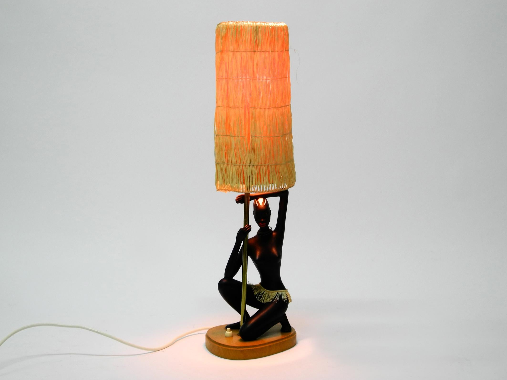 Beautiful very rare original midcentury Cortendorf ceramic table lamp.
Very fine African female body down on one knee on a wooden base.
Very high quality with many nice details. Original lampshade made of raffia. Made in West Germany.
Very good