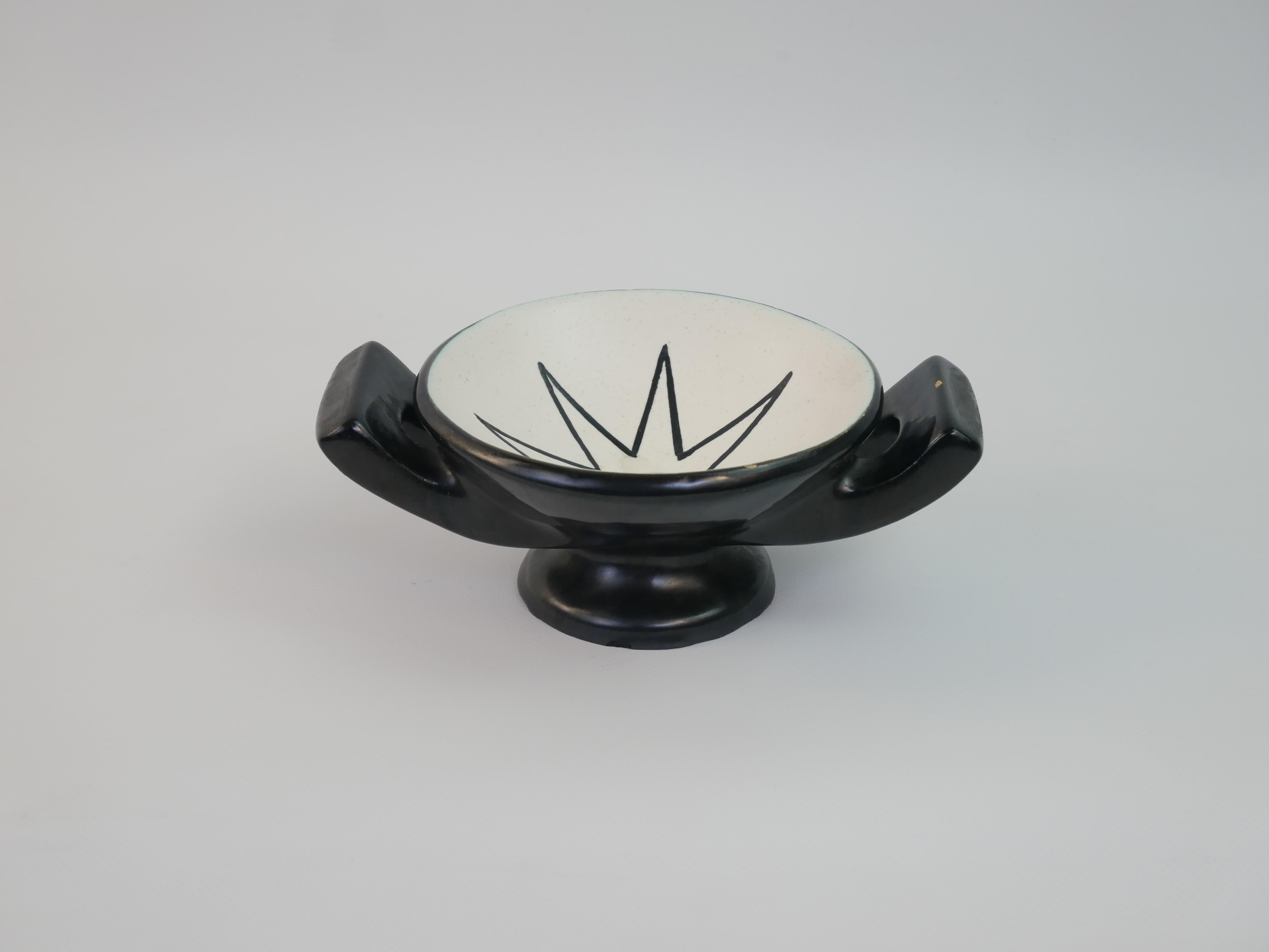
This ceramic vide-poche, attributed to Robert Picault, features his distinctive Vallauris craftsmanship. The piece is characterized by its black-glazed exterior and white interior, adorned with graphic motifs. One design includes a starburst