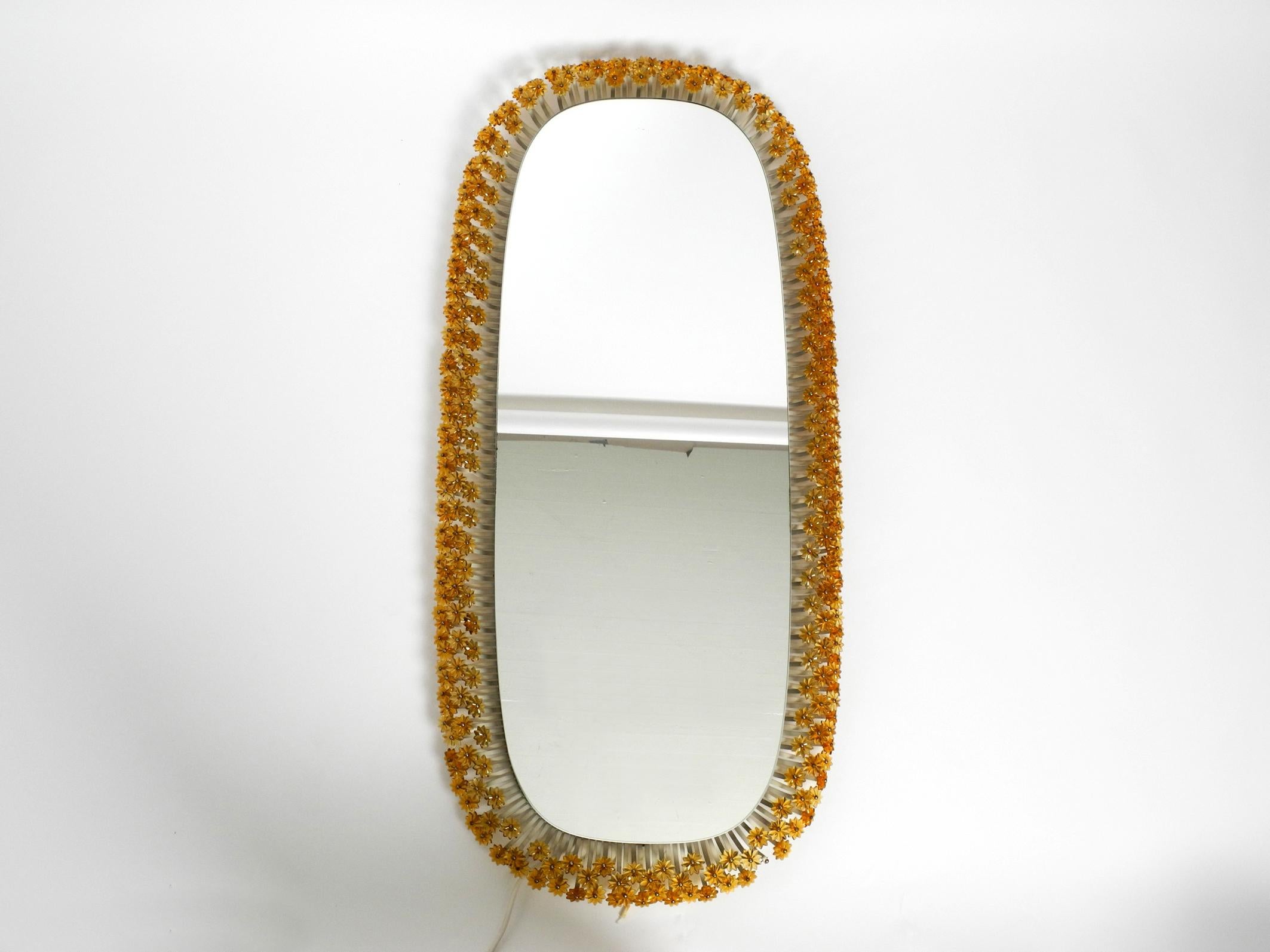 Wonderful rare XXXL backlit Mid-Century Modern flower mirror by Münchner Zier-Form. Manufacturer is Schöninger Spiegel. Made in Germany.
Great elaborate design with many small plastic flowers in amber color. 
The back is made of wood and is