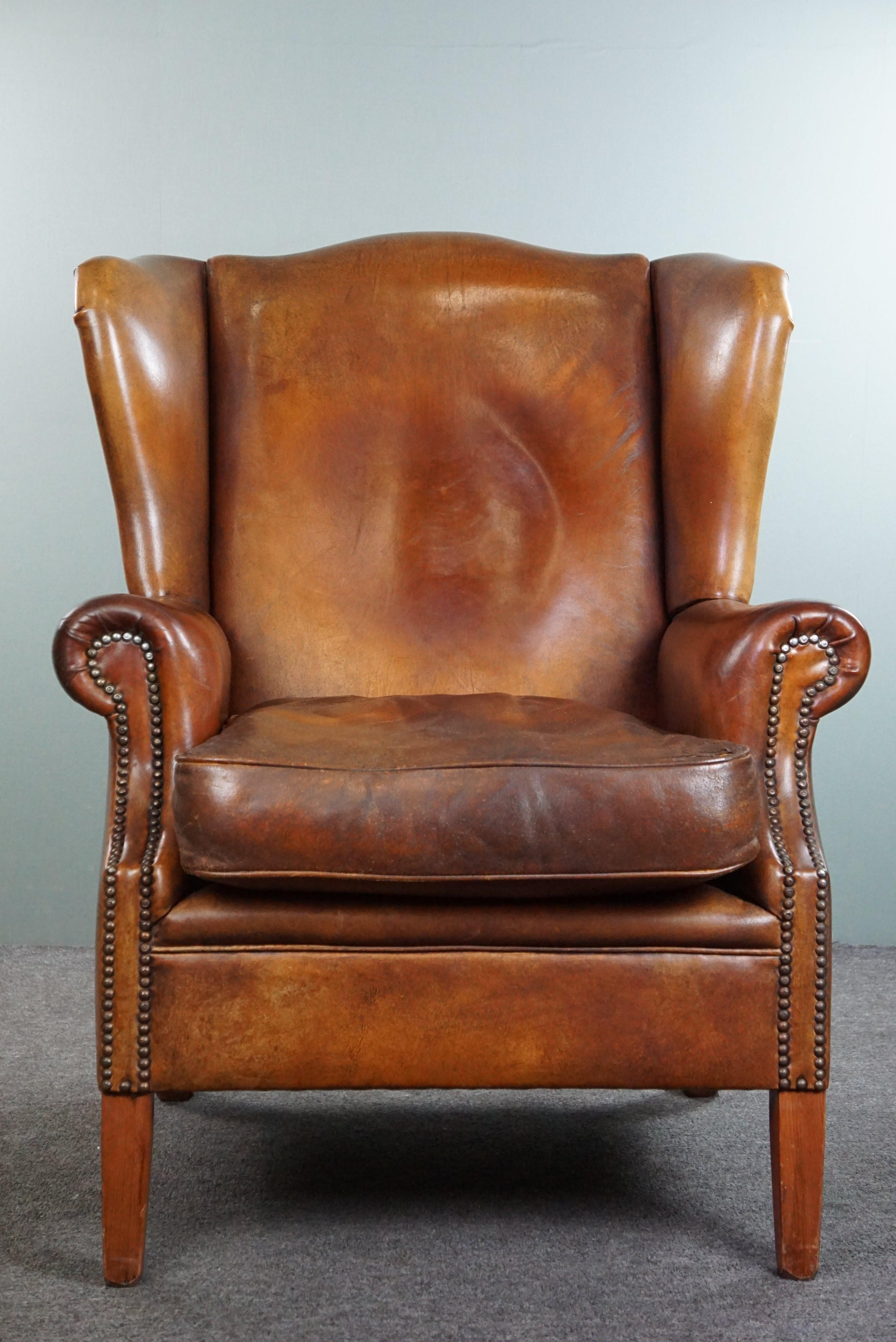 Offered is this very rugged yet comfortable wingback armchair made of cognac-colored sheep leather finished with decorative nail heads. 

Despite its rugged appearance, this is still a wonderfully comfortable armchair to relax in for hours. Even as