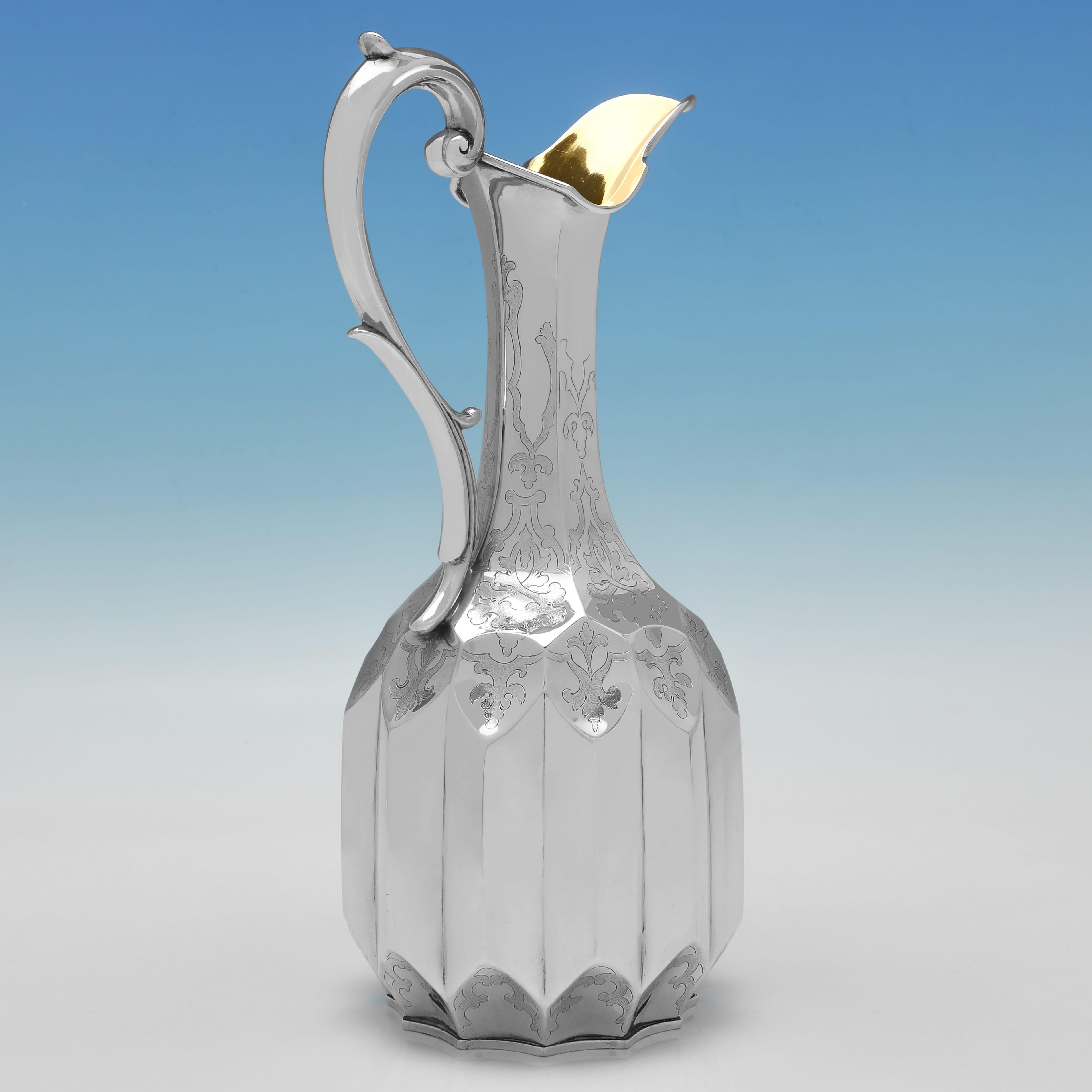 Hallmarked in London in 1851 by Joseph Angell, this stylish, Victorian, Antique Sterling Silver Wine Ewer, features shaped sides with engraved detailing, a scroll handle, and a gilt interior. The wine ewer measures 10.25