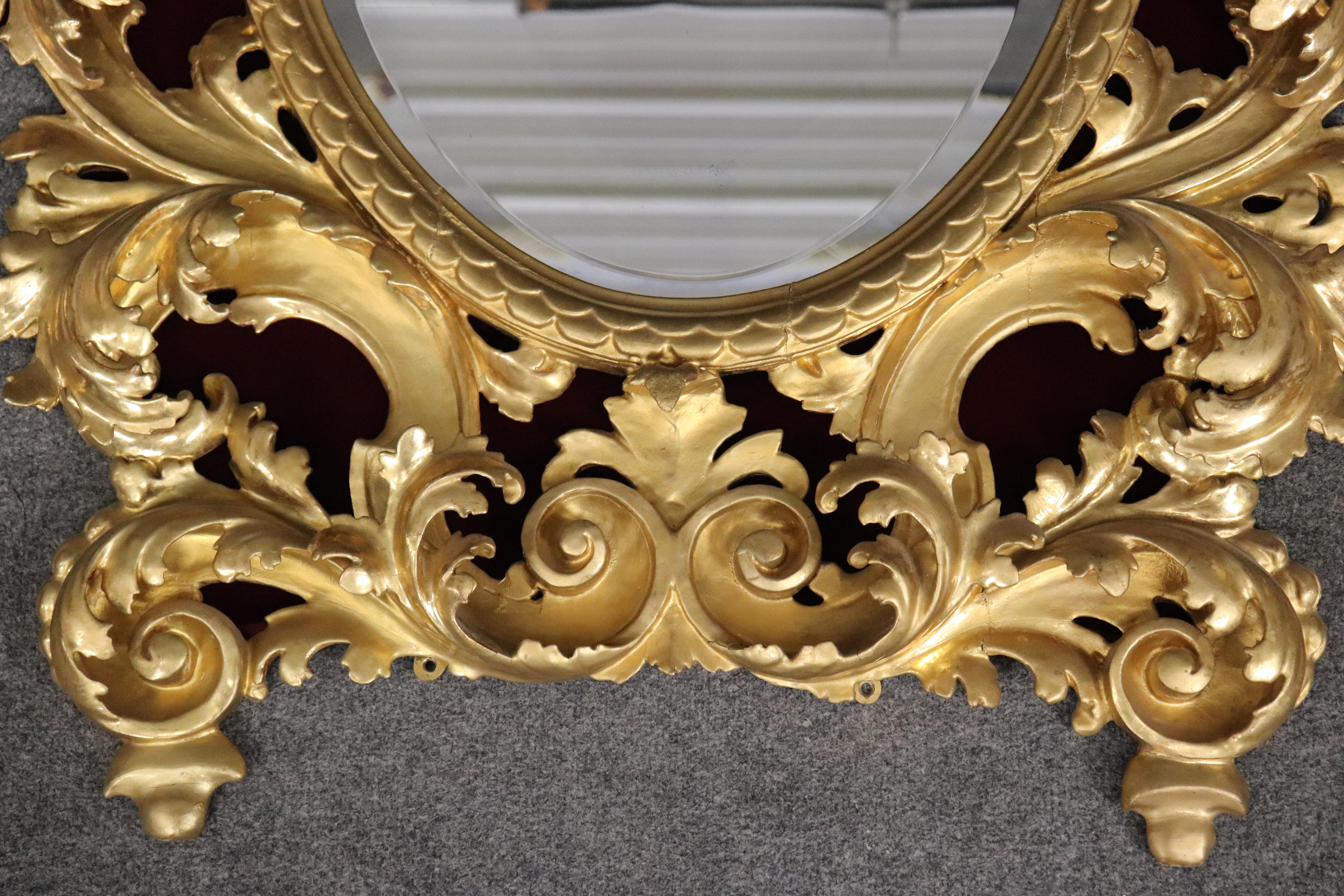 This is a very large and rare form of Florentine mirror made in Italy with a beveled glass mirror plate. The mirror is profusely carved with ornate stylized leaf and foliage and gilded in gold leaf. As with most of these mirrors due to the extremely