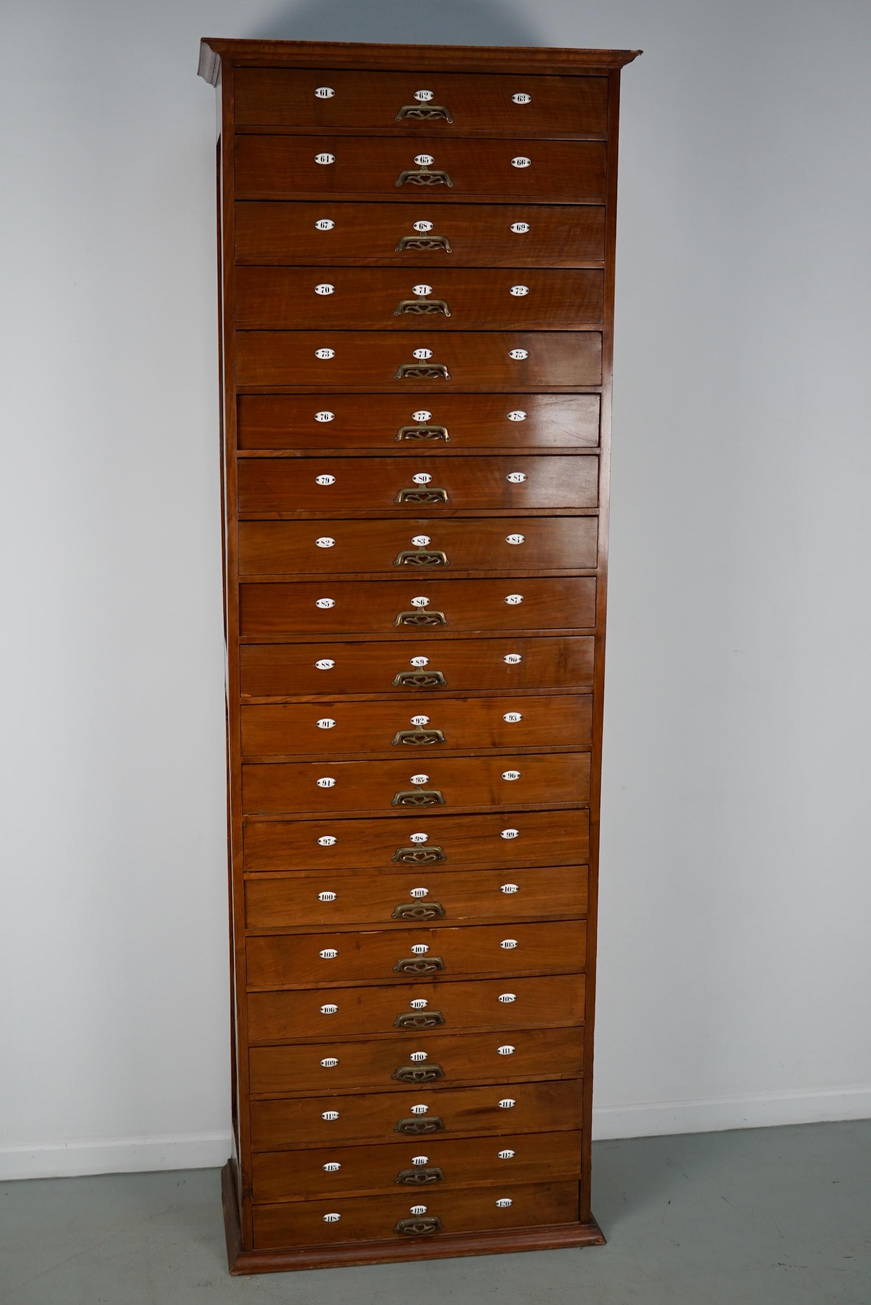 Cette armoire d'apothicaire a été fabriquée vers les années 1900 aux Pays-Bas. Il comprend 20 tiroirs avec d'étonnantes poignées ornées en laiton et des numéros en émail. Il a été conçu à l'origine pour un barbier et servait à ranger les accessoires