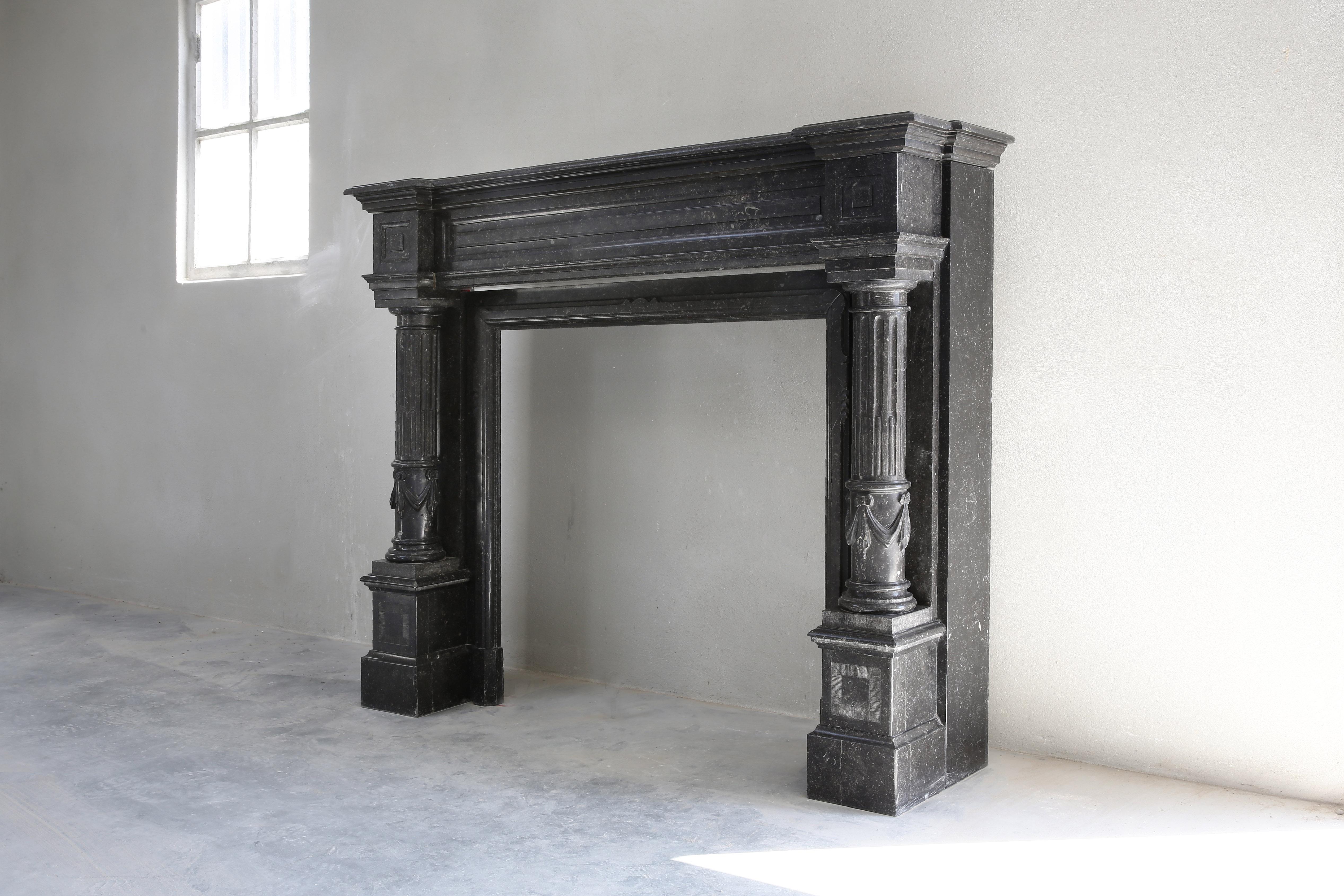 A special fireplace with many adaptations in the neoclassical style from the 19th century. The top has beautiful lines and various ornaments. The legs are partially round and equipped with flutes. A stately fireplace made of Belgian bluestone that
