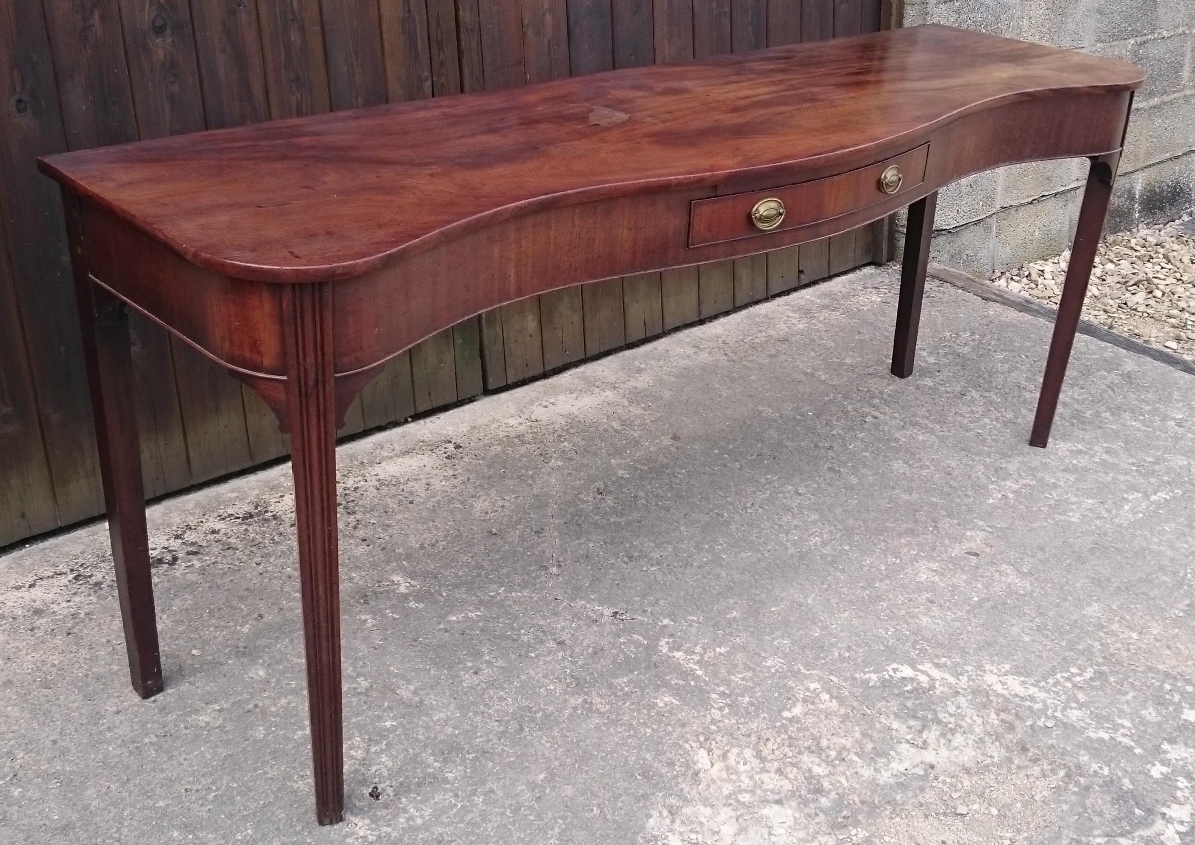 18th century George III period mahogany antique serving table with serpentine front and square taper legs. The top of this serving table is made of a single huge sheet of timber that has faded to a perfect golden honey colour. This table is pictured