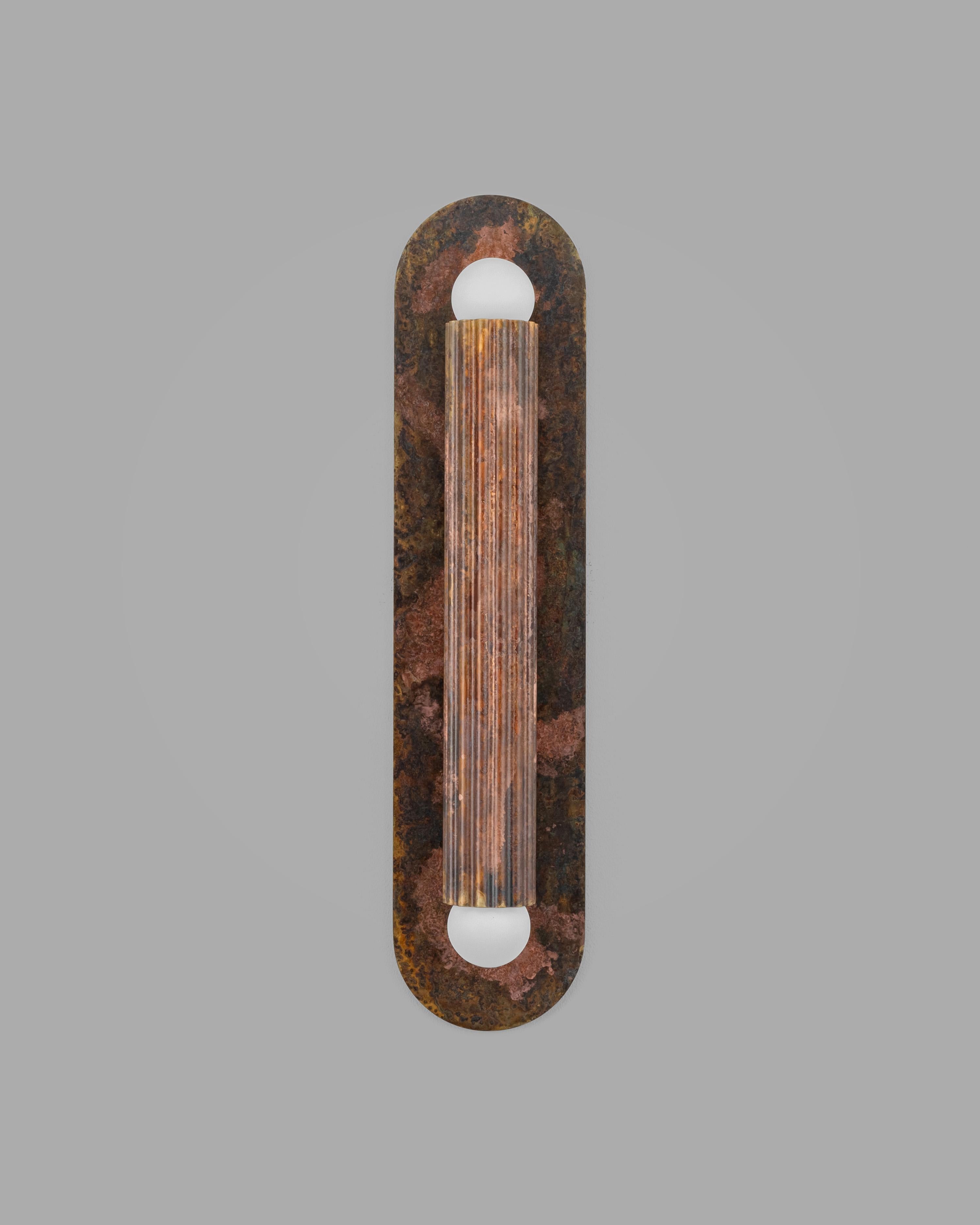 Un cylindre cannelé unique repose sur une plaque ovale, sa géométrie distillée jusqu'à la forme pure. Entièrement réalisée en laiton massif, elle capte la lumière qui ondule sur les lignes verticales, apportant chaleur, profondeur et intensité