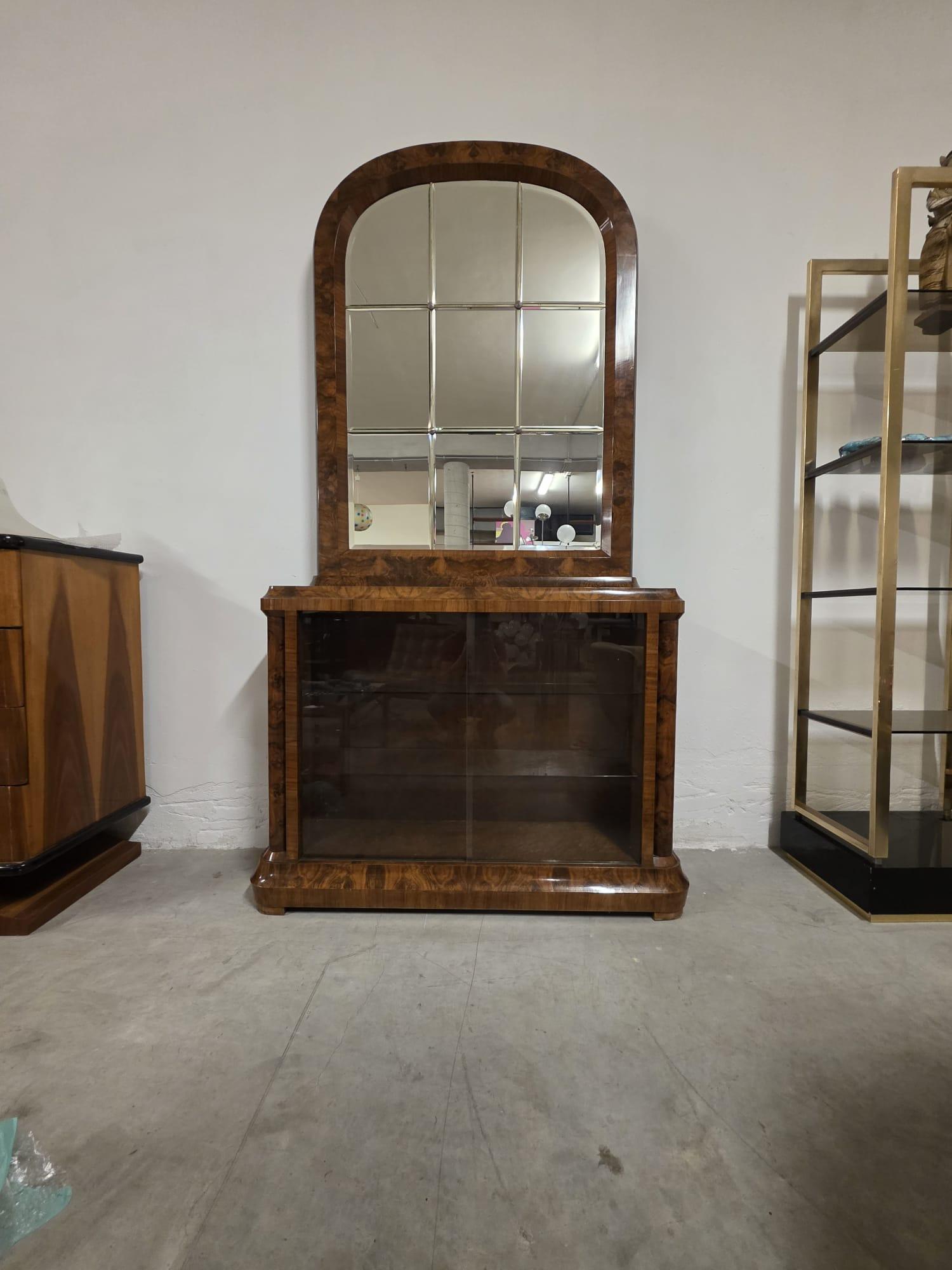 Art Deco burl display case.

Elegant walnut-root display case from the 1930s.

At the bottom are two sliding glass doors with two glass tops inside.

The upper part features a large arched mirror with beveled glass and briarwood frame.

Refined and