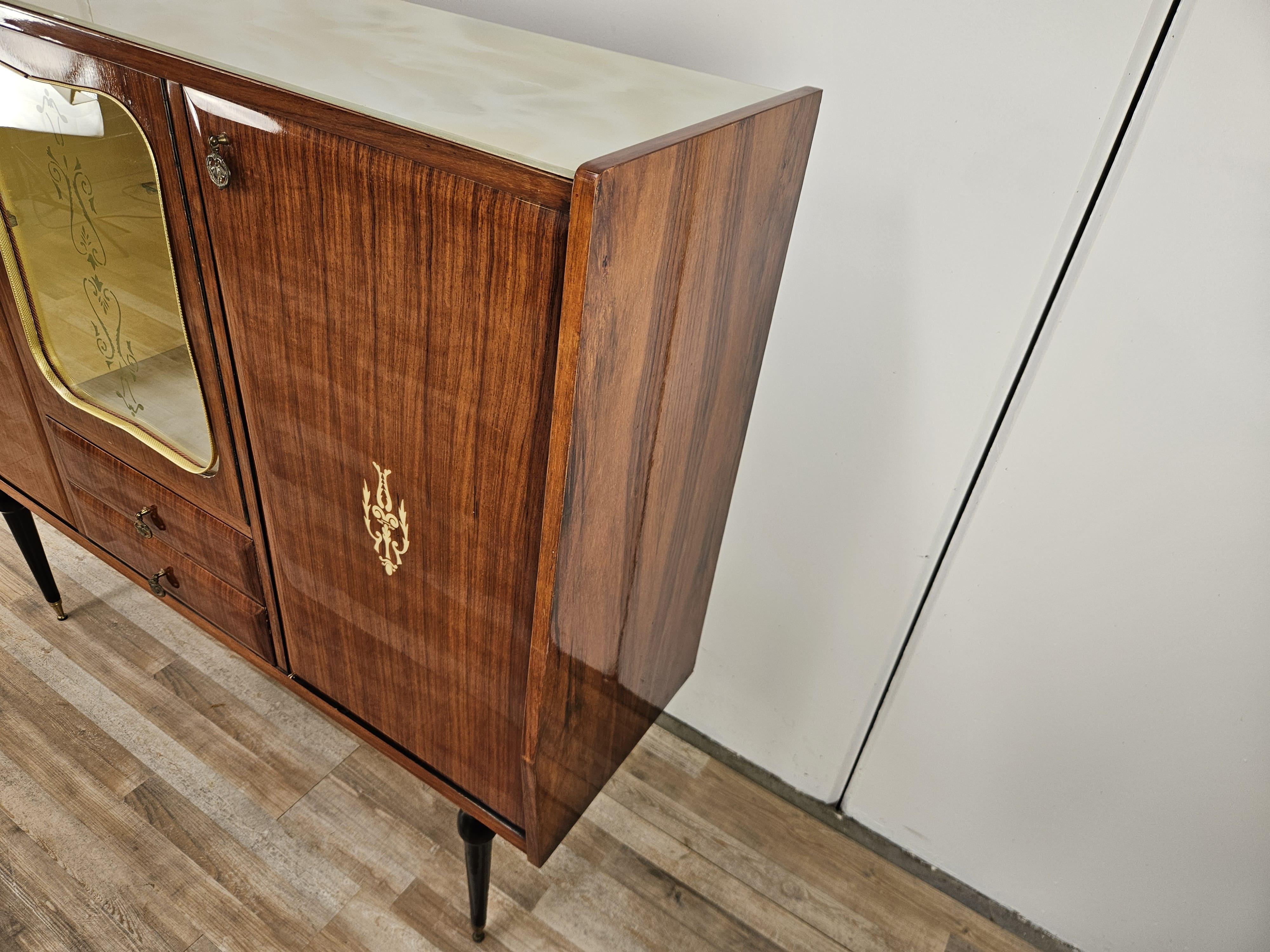Sideboard with center display case 1960s for dining room hallway or living room, upholstered in mahogany with two side doors and a pair of drawers in the center.
Note the beautiful finely crafted glass door with interior shelf and mirrored bottom.