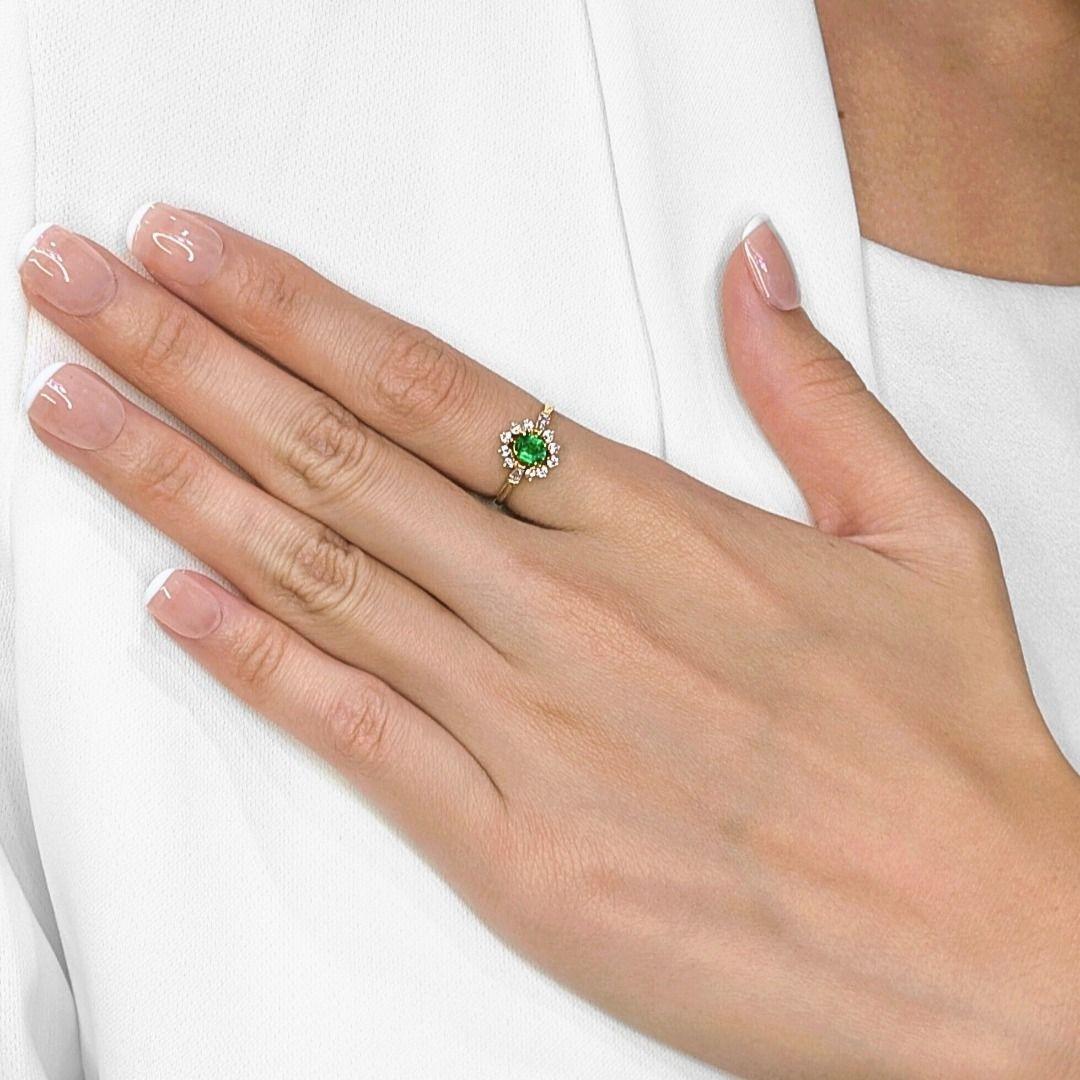Dieser Ring strahlt zeitlose Schönheit aus mit seinem lebendigen 0,28-cm-Smaragd im Ovalschliff, der in der Mitte in einem satten Grünton leuchtet. Der Smaragd wird von einem leuchtenden Halo aus 10 runden Brillanten und 2 Diamanten im Kegelschliff