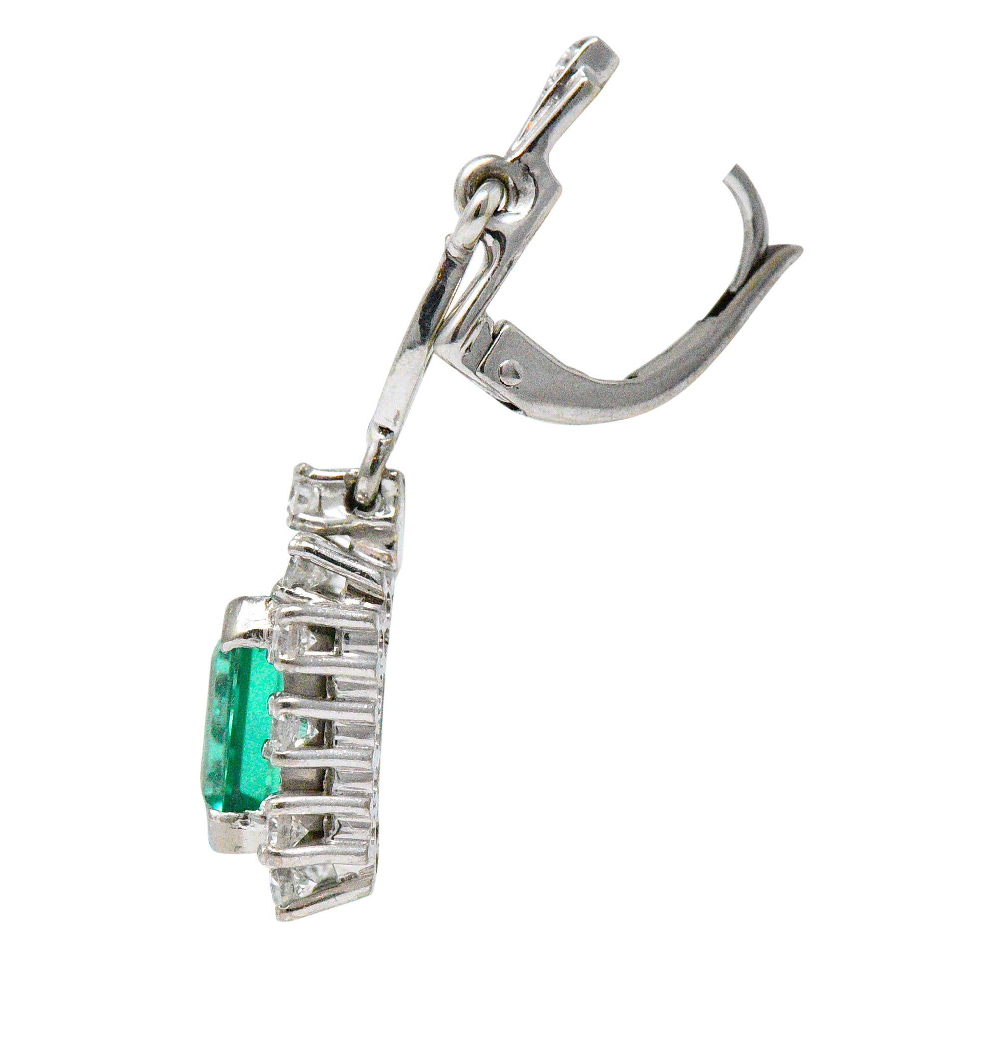 Designed as lever back style earrings suspending articulated cluster drops

Each centers emerald cut Colombian emeralds weighing in total 3.96 carats; transparent and strikingly green in color with only minor clarity enhancement (oil) 

Surrounded