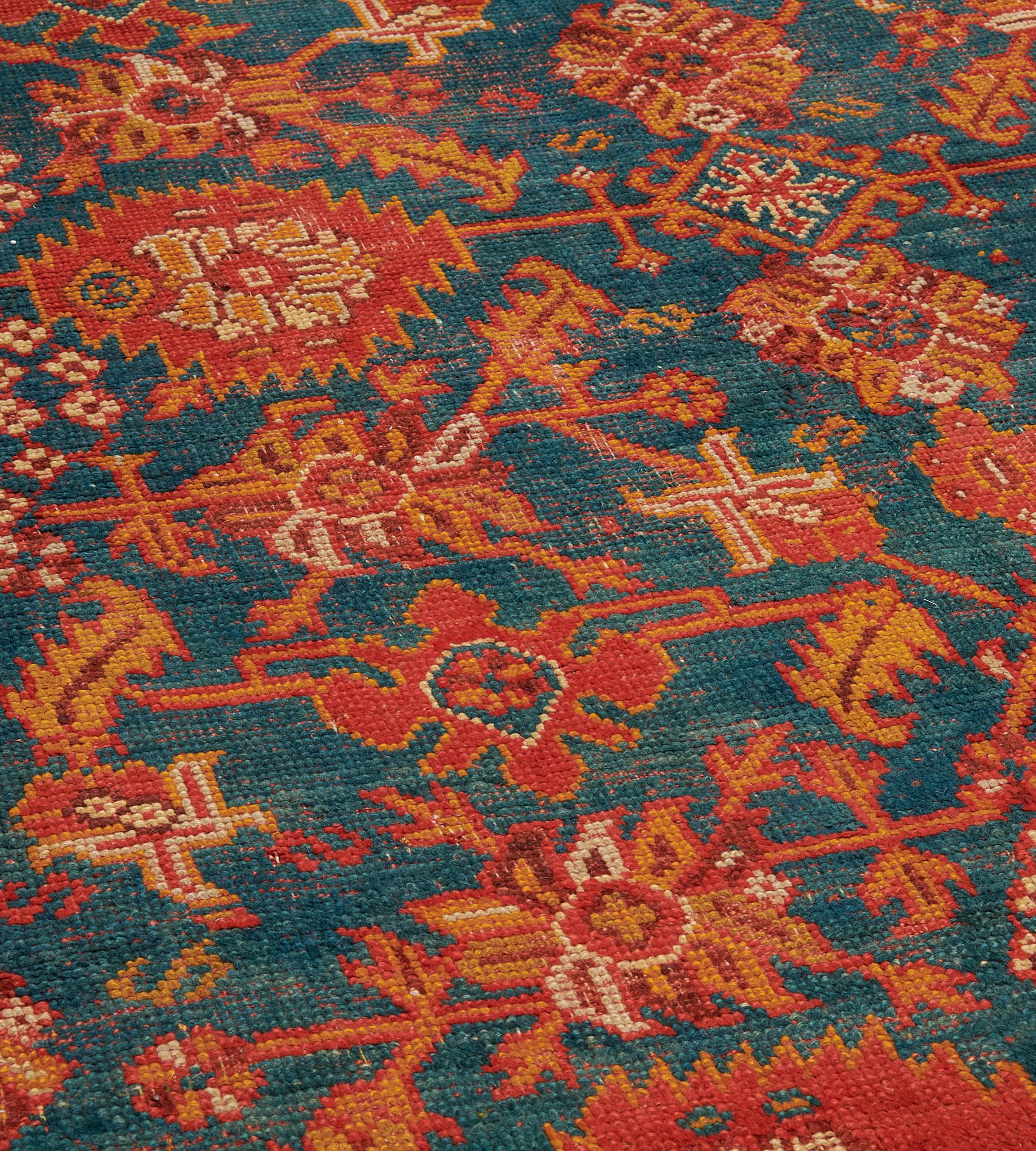 Dieser traditionelle, handgewebte türkische Oushak-Teppich hat ein schattiertes, blaues Feld mit einem Gesamtmuster aus tomatenroten, feuerorangen und elfenbeinfarbenen Palmetten und eckigen Blumen- und Blattranken in einer feuerorangenen Bordüre