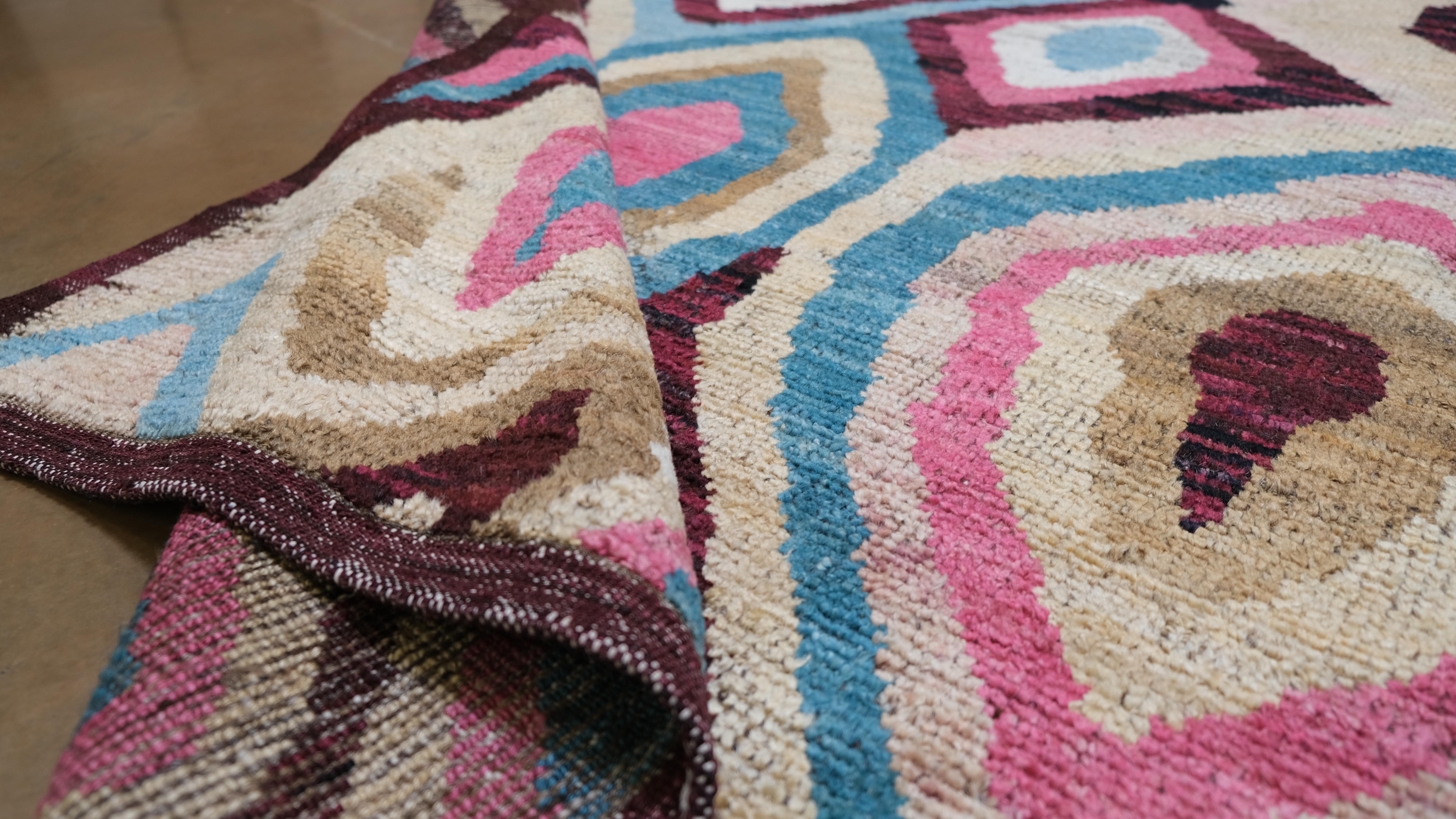  Featuring a bold and vibrant geometric abstract design, this rug showcases an array of rich colors, including pink, blue, beige, and brown, arranged in a captivating layered pattern. The lively and artistic motif makes this piece a statement