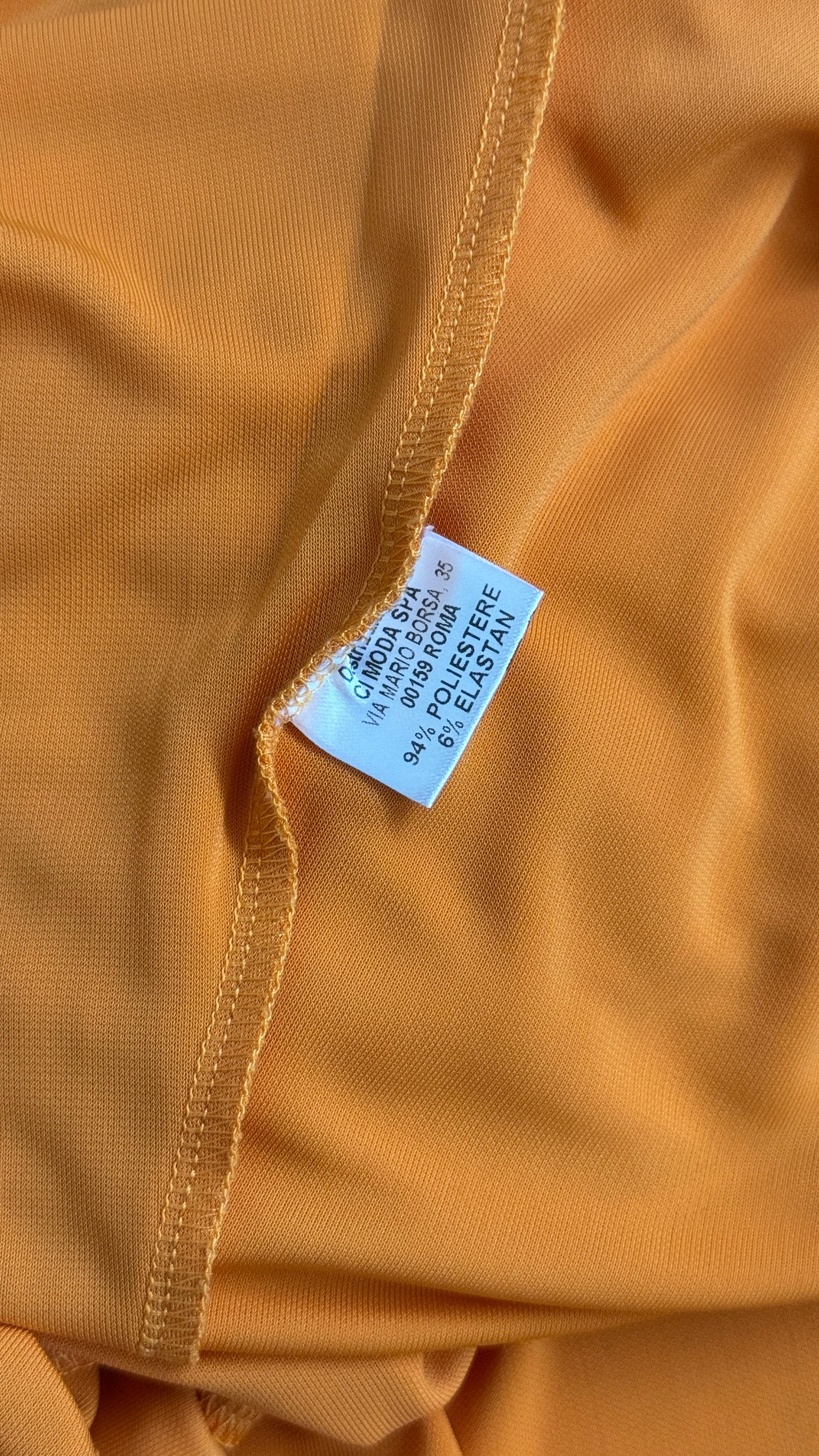 Cette robe bodycon orange est conçue par Compagnia Italiana, une célèbre marque de mode italienne qui a connu une grande popularité dans les années 1990 et 2000. Fabriquée en Italie, cette robe présente une silhouette élégante et un tissu extensible
