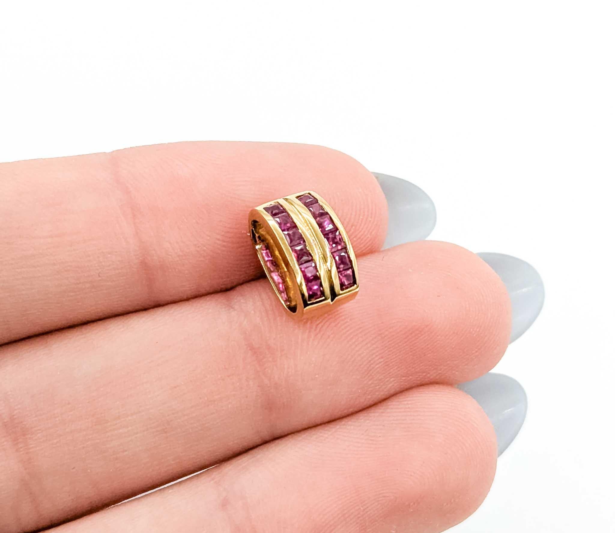 Este elegante colgante está engastado con aproximadamente 0,36 quilates de peso total de rubíes de talla cuadrada, dispuestos en dos filas de canales que resaltan el vivo tono rojo de las piedras. El rico engaste de oro amarillo de 18 quilates