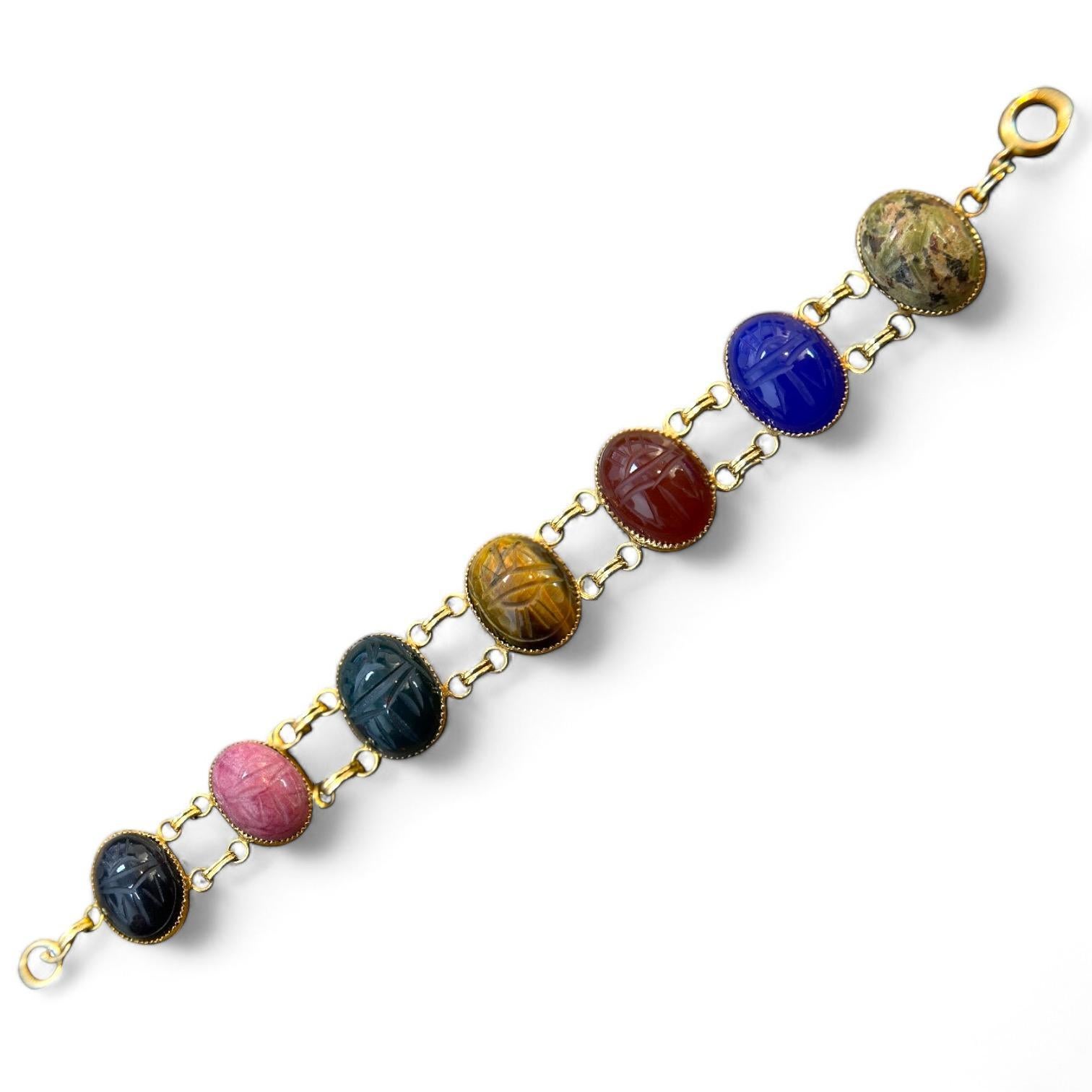 Ornez votre poignet avec ce superbe bracelet composé de sept pierres de forme ovale sculptées de façon complexe avec des motifs de scarabées. Chaque pierre aux couleurs vives présente un spectre de teintes à couper le souffle : noir riche, rose
