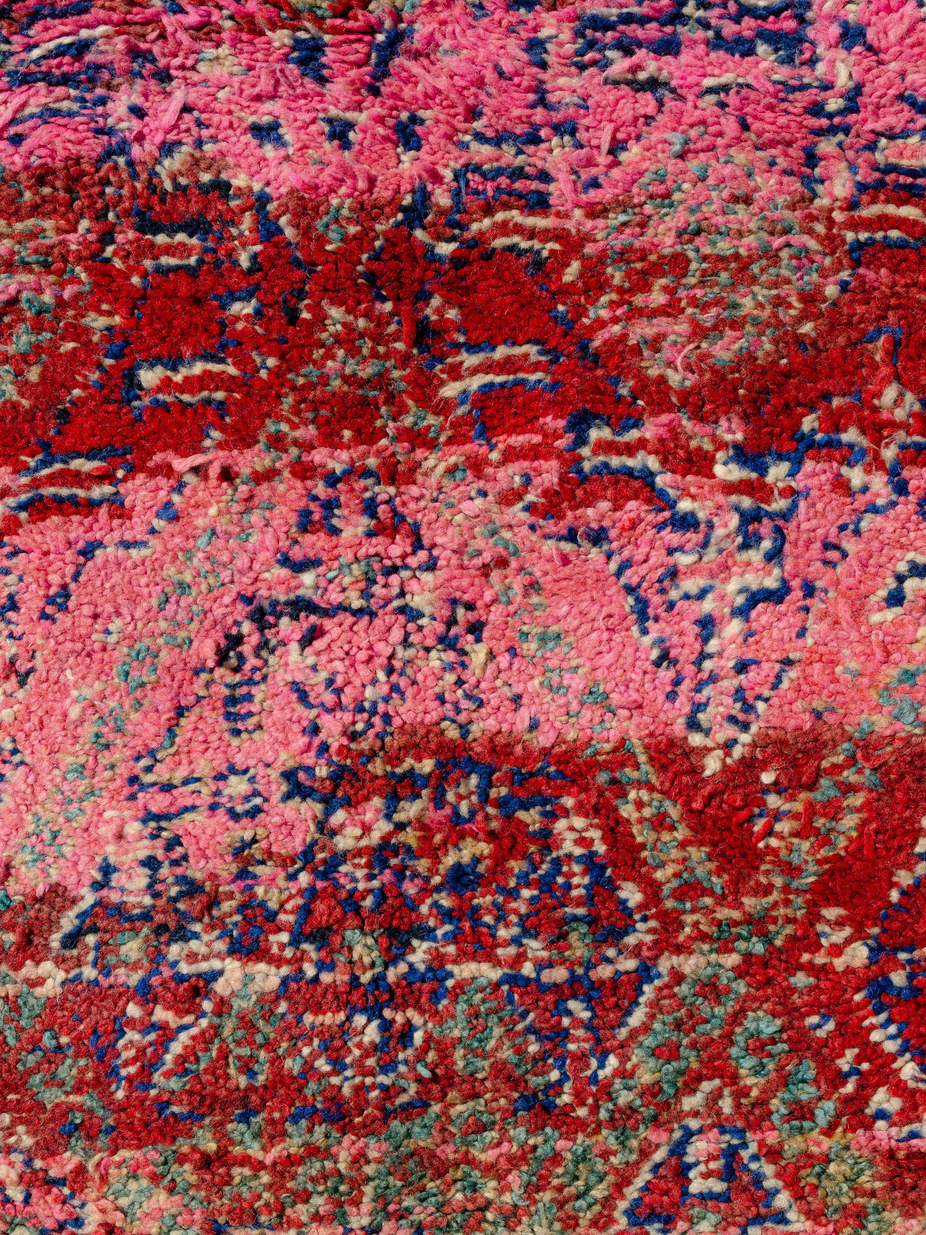 A vintage Moroccan Beni M'Guild featuring vivid pink striations alternating with scarlet and burgundy creating a striking rhythm. The diffuse motifs knotted in cobalt and celadon appear pixelated, lending subtlety to the weaver’s colorful message.