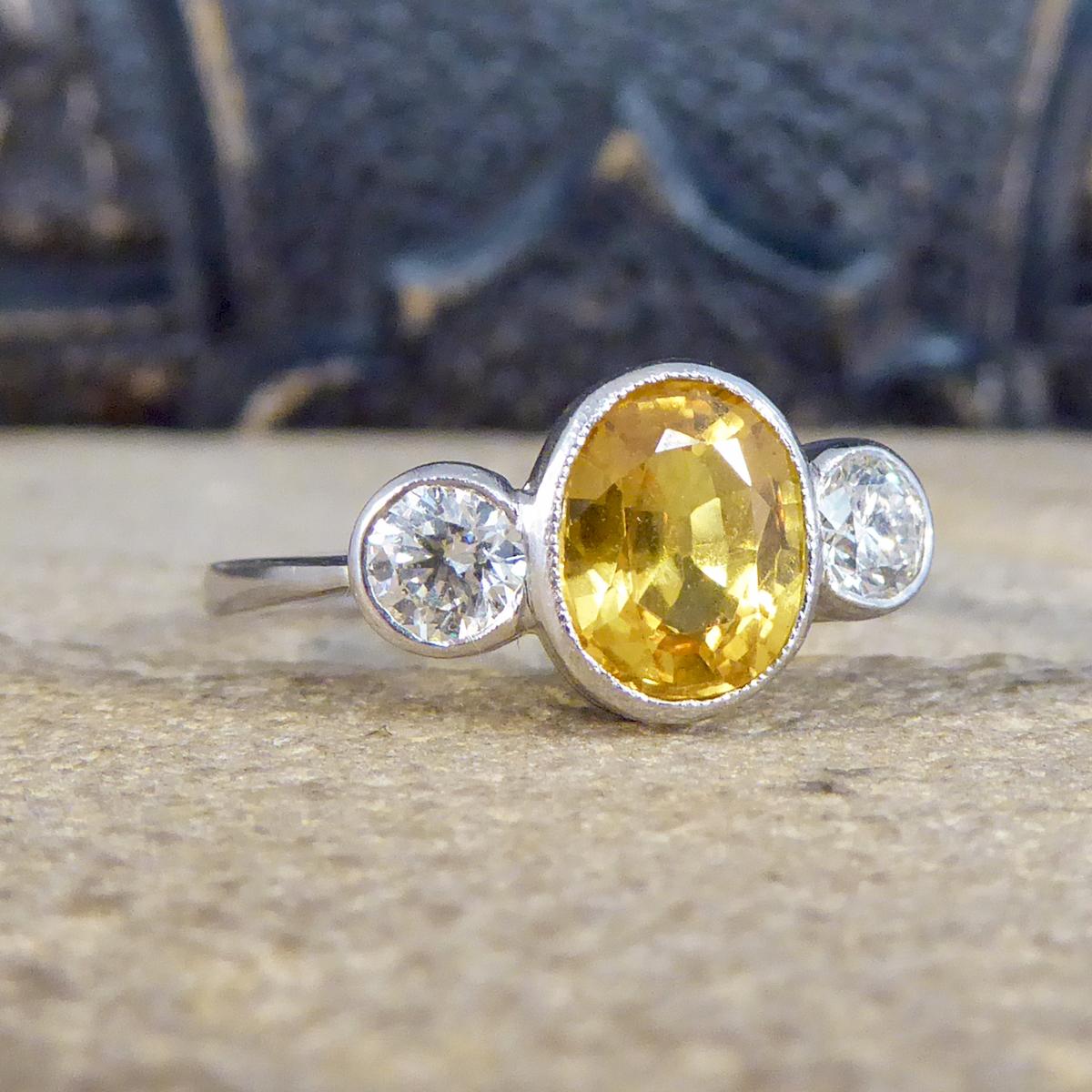 A very elegant three stone ring that is set with a beautifully vibrant Yellow Sapphire in the centre weighing 1.80ct with two bright and clear round cut Diamonds on either side in a collar setting. This ring has been crafted and set in Platinum, a