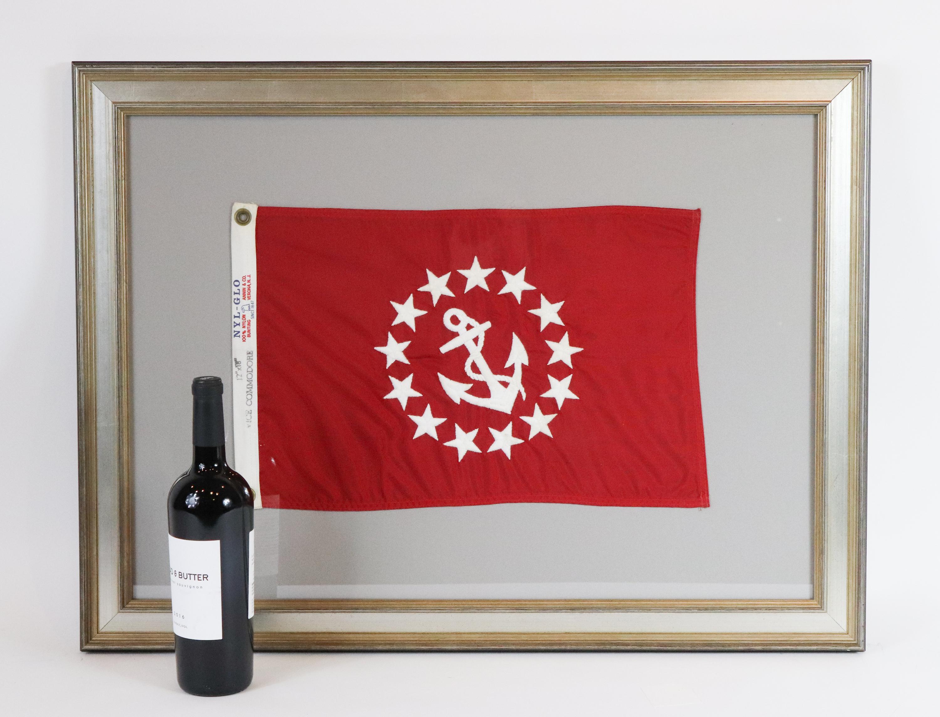 Framed Vice Commodore flag showing a red field with a white embroidered fouled anchor surrounded by a ring of stars. Nicely framed with gray mat. Measures: 32