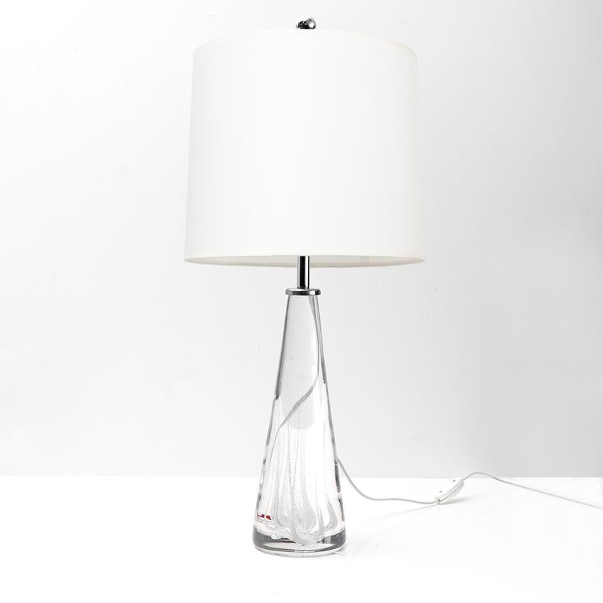 A Scandinavian Modern solid crystal glass table lamp made by one of Sweden's top glass producers, Kosta. The lamp is detailed with internal streaks of air bubbles and fitted with polished steel hardware and a single standard base 3-way socket newly