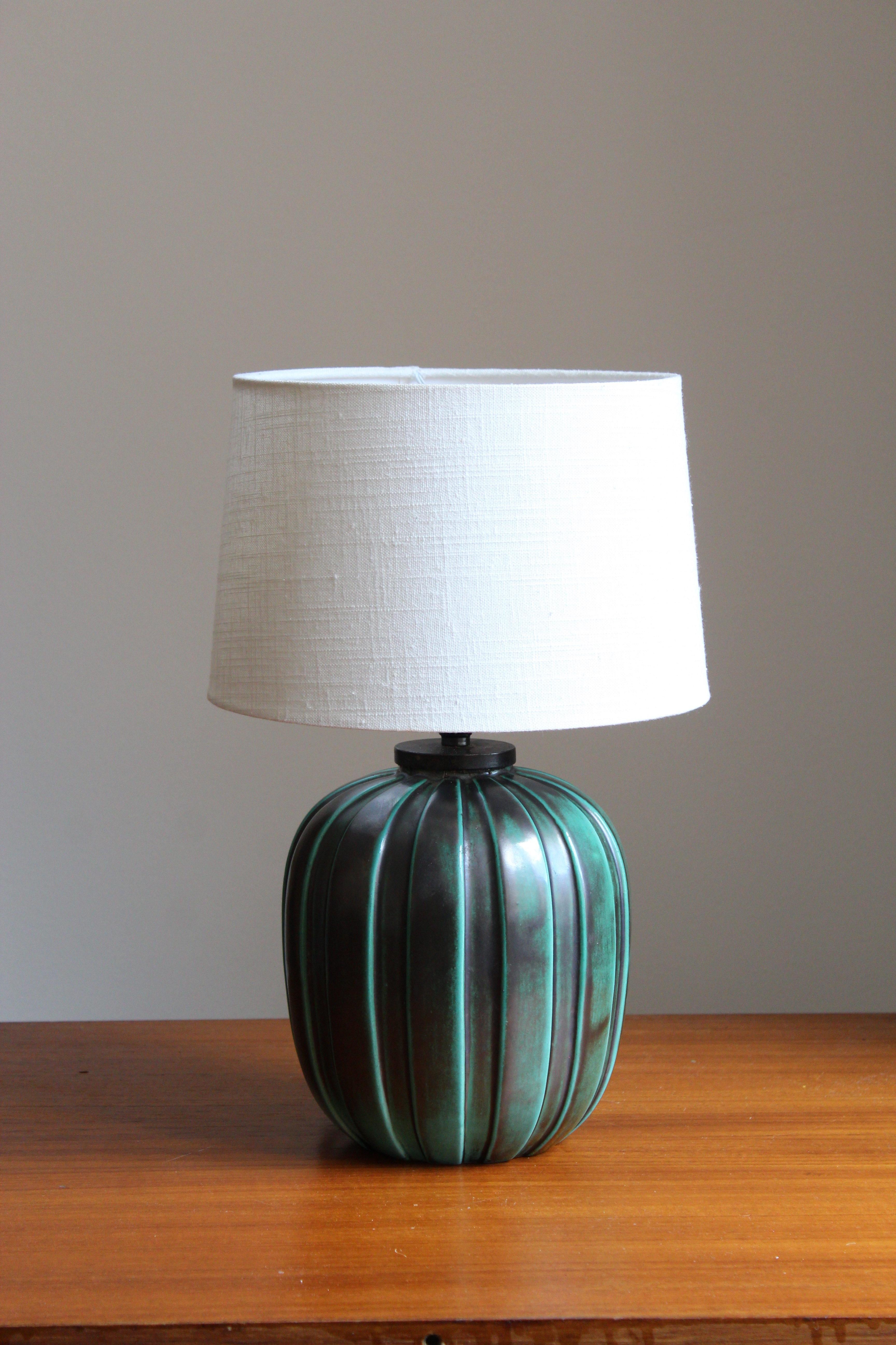 An early modernist table lamp. Designed by Vicke Lindstrand, for Upsala-Ekeby, Sweden, 1940s. Stamped and with production label.

Sold without lampshade, stated dimensions excluding lampshade.

Glaze features a blue-green color and black.

Other